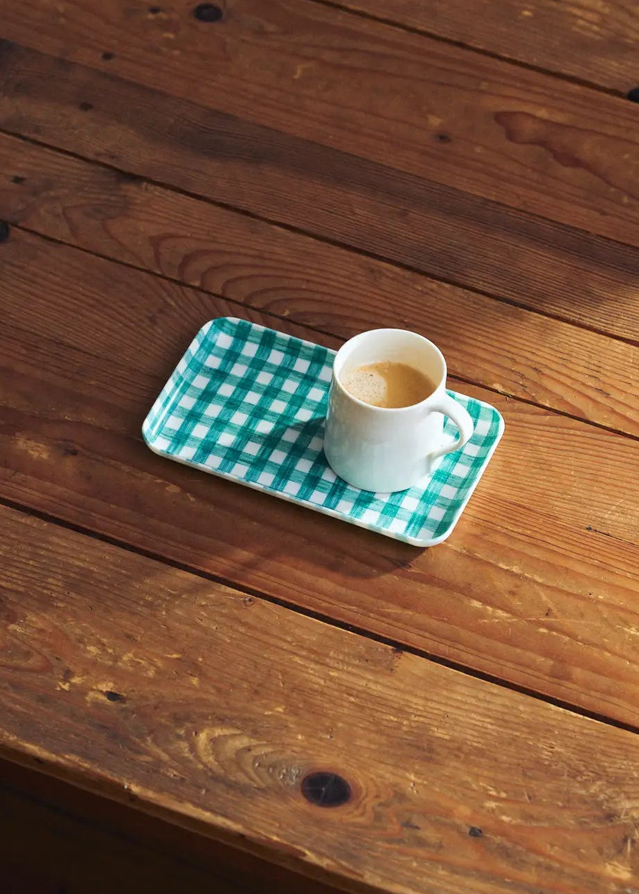 White cup with green checkered coaster on a wooden surface