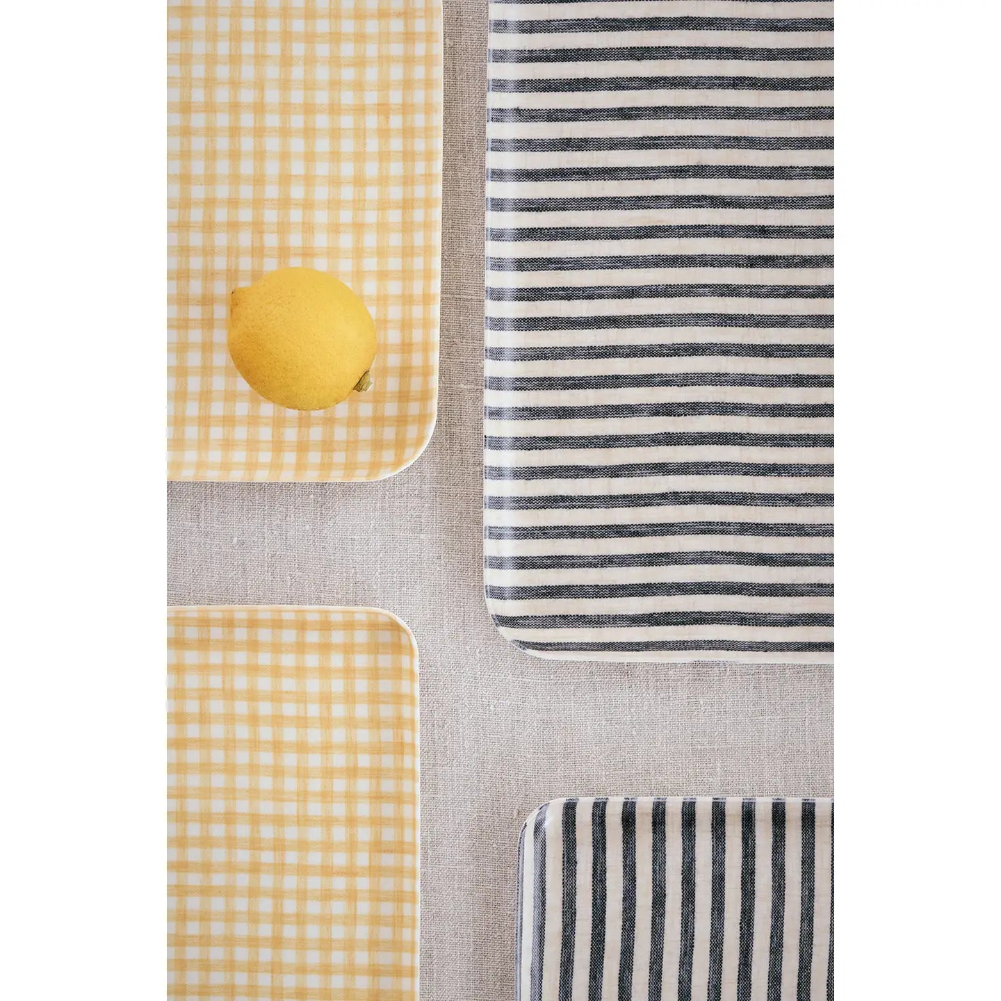 Three rectangular fabric trays  with rounded corners arranged on a light gray textured surface. Two have a yellow-and-white gingham pattern, and one has dark gray-and-white horizontal stripes.
