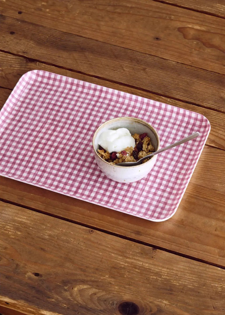 Pink checkered tray with a bowl of cereal on a wooden surface