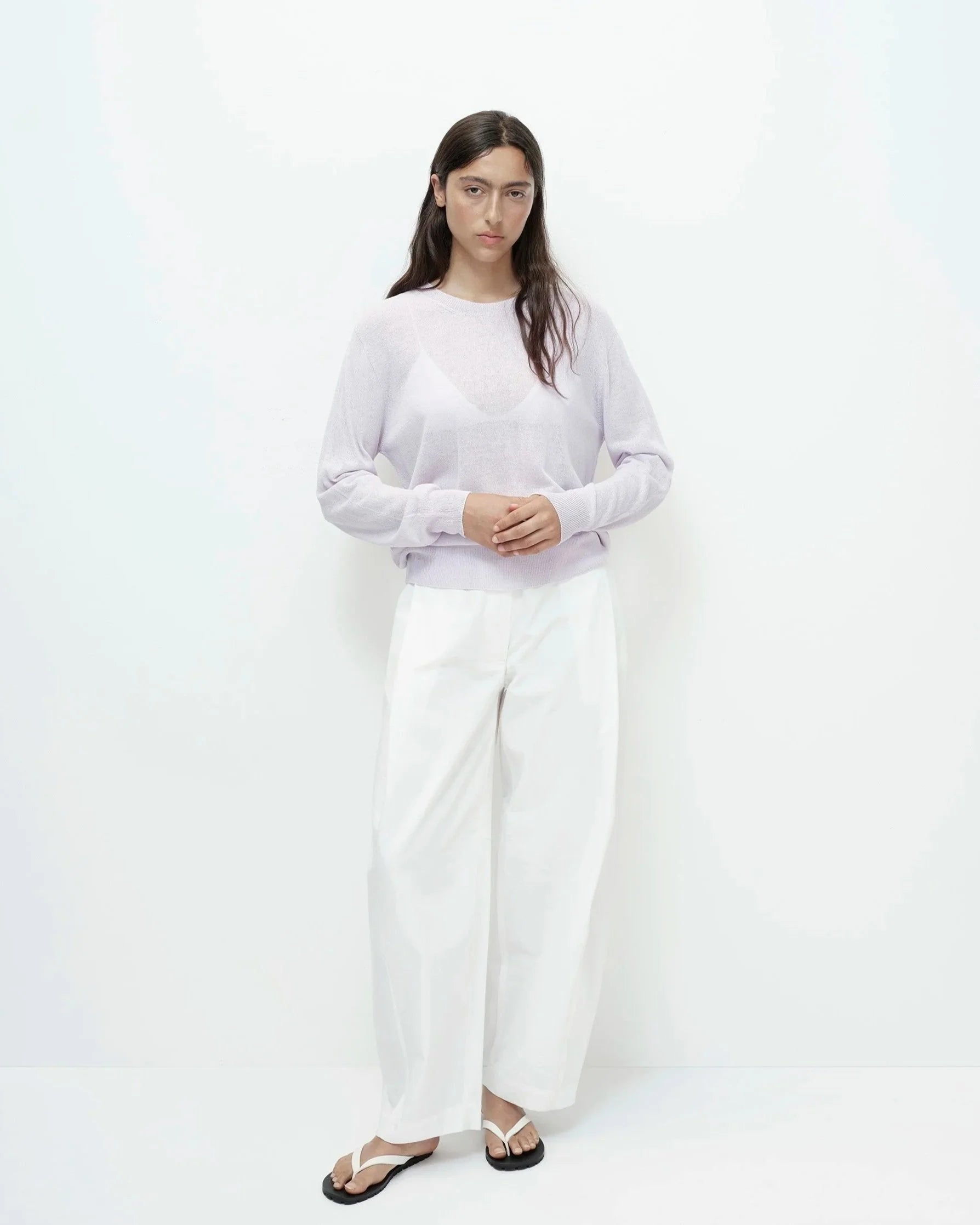 Woman wearing a light purple sweater and white pants on a white background