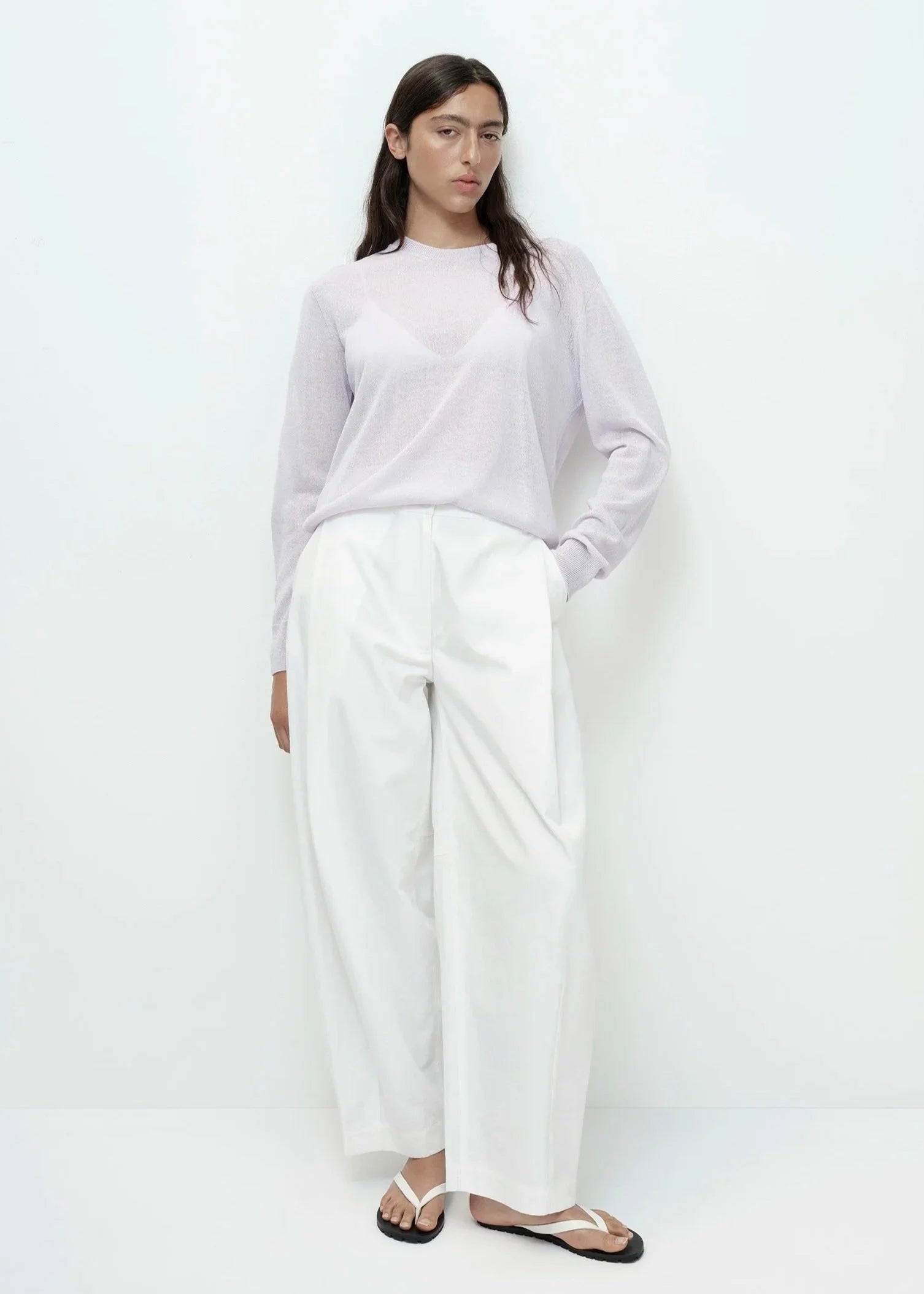 Woman wearing a light purple sweater and white pants on a white background