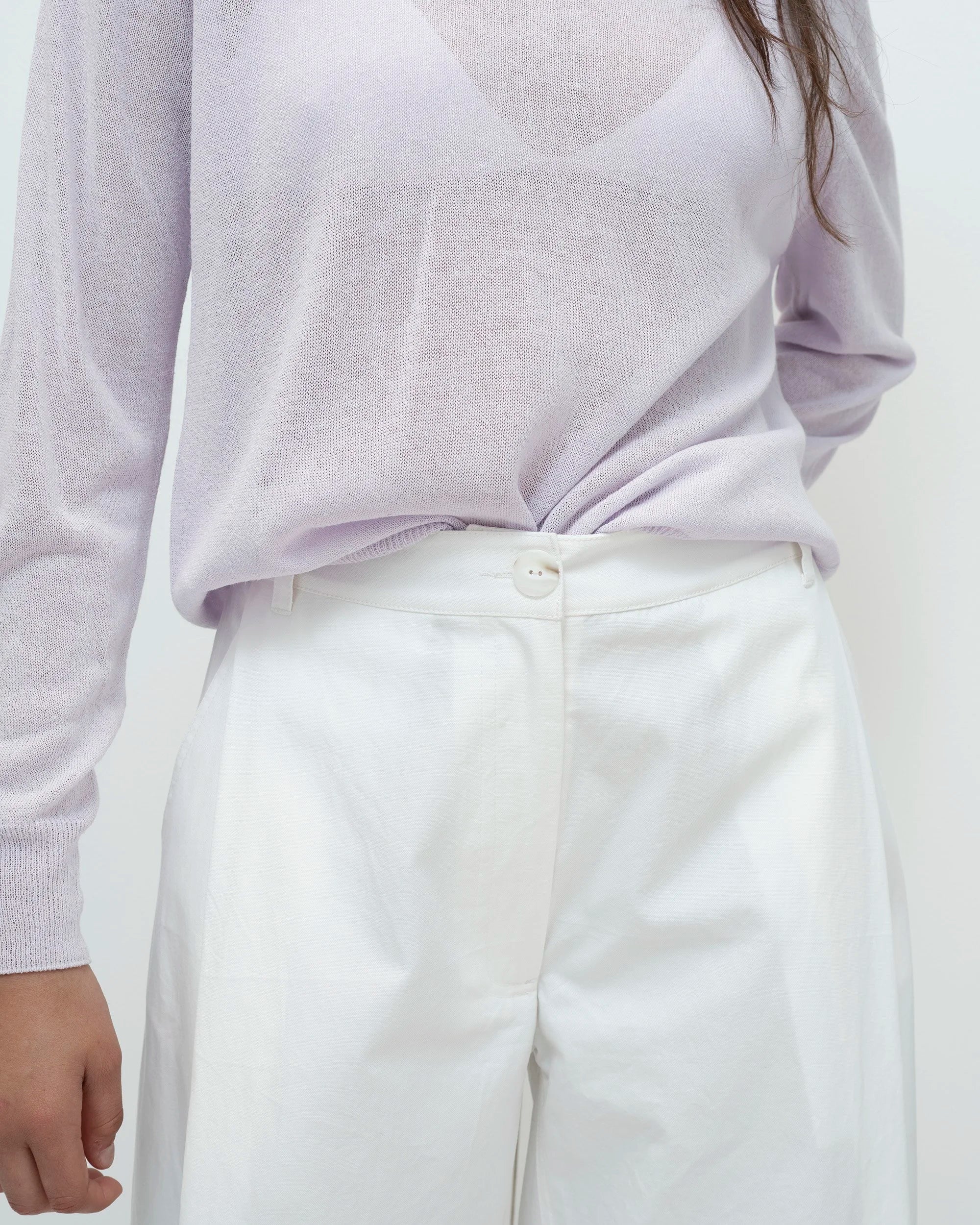 Woman wearing a light purple sweater and white pants on a white background