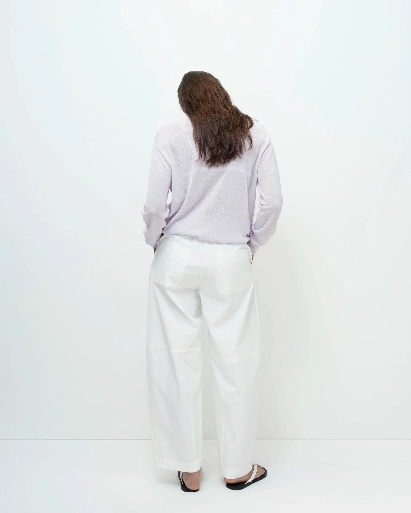 Woman wearing a light purple sweater and white pants on a white background