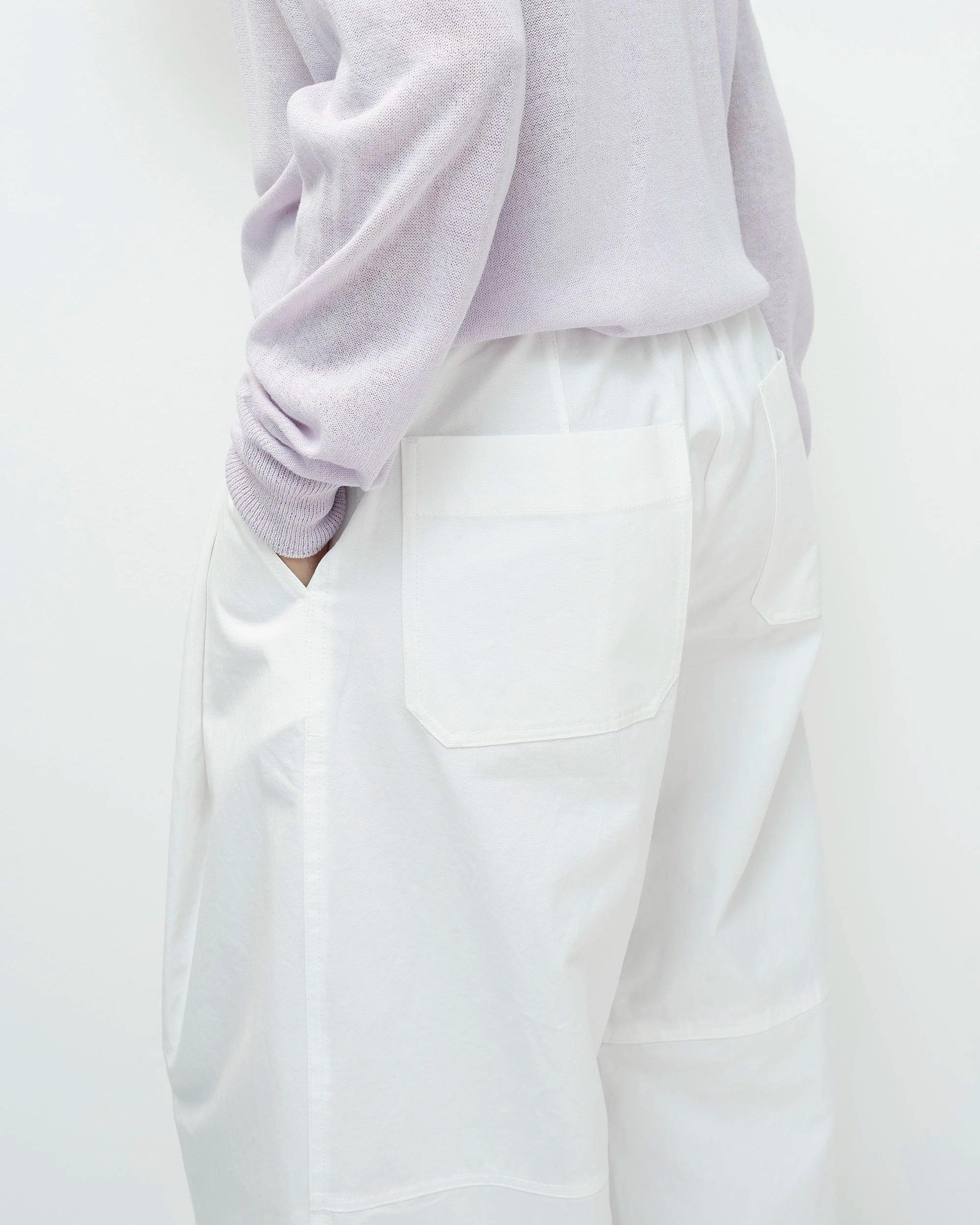 Woman wearing a light purple sweater and white pants on a white background