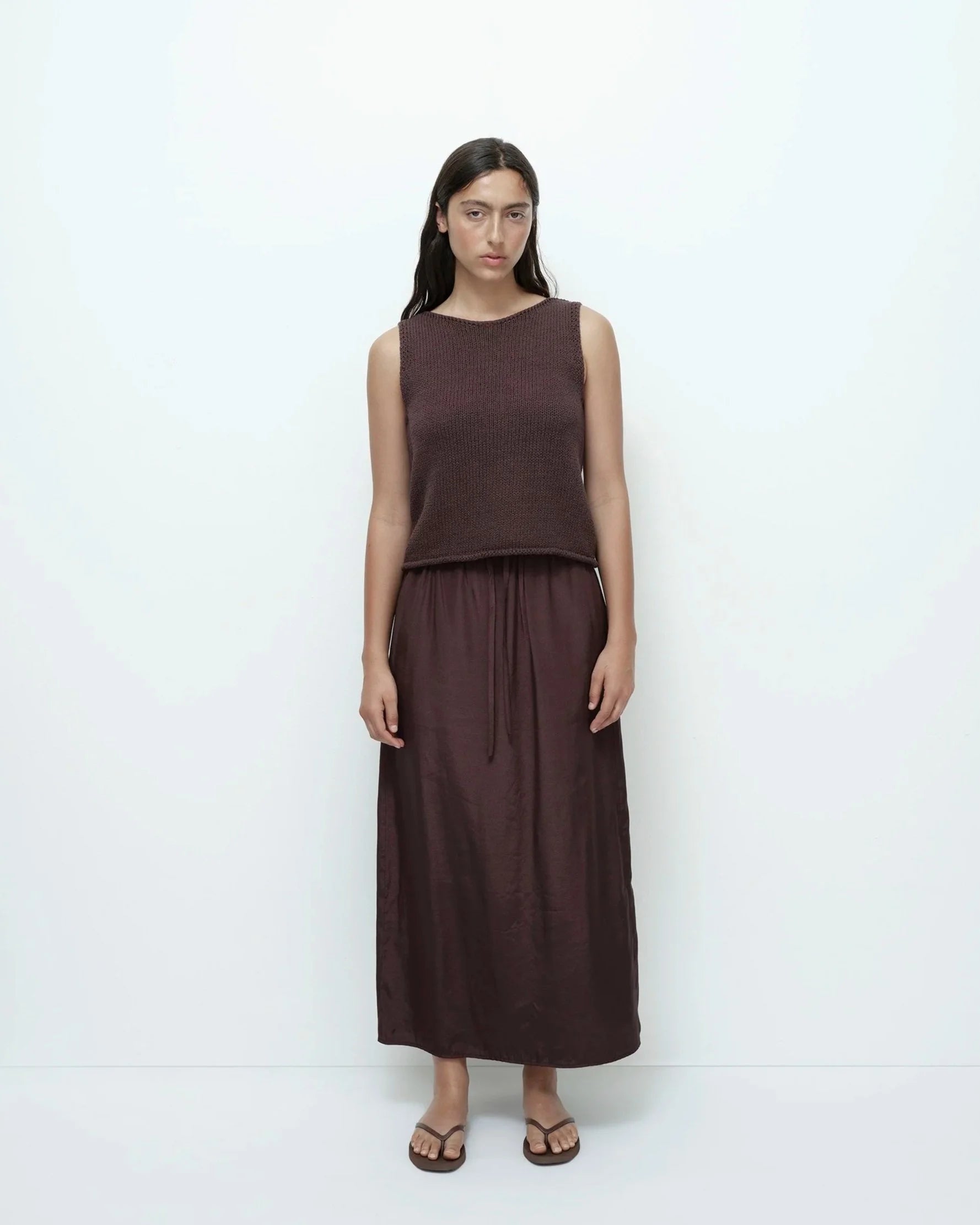 Woman wearing a brown sleeveless top and long skirt against a white background