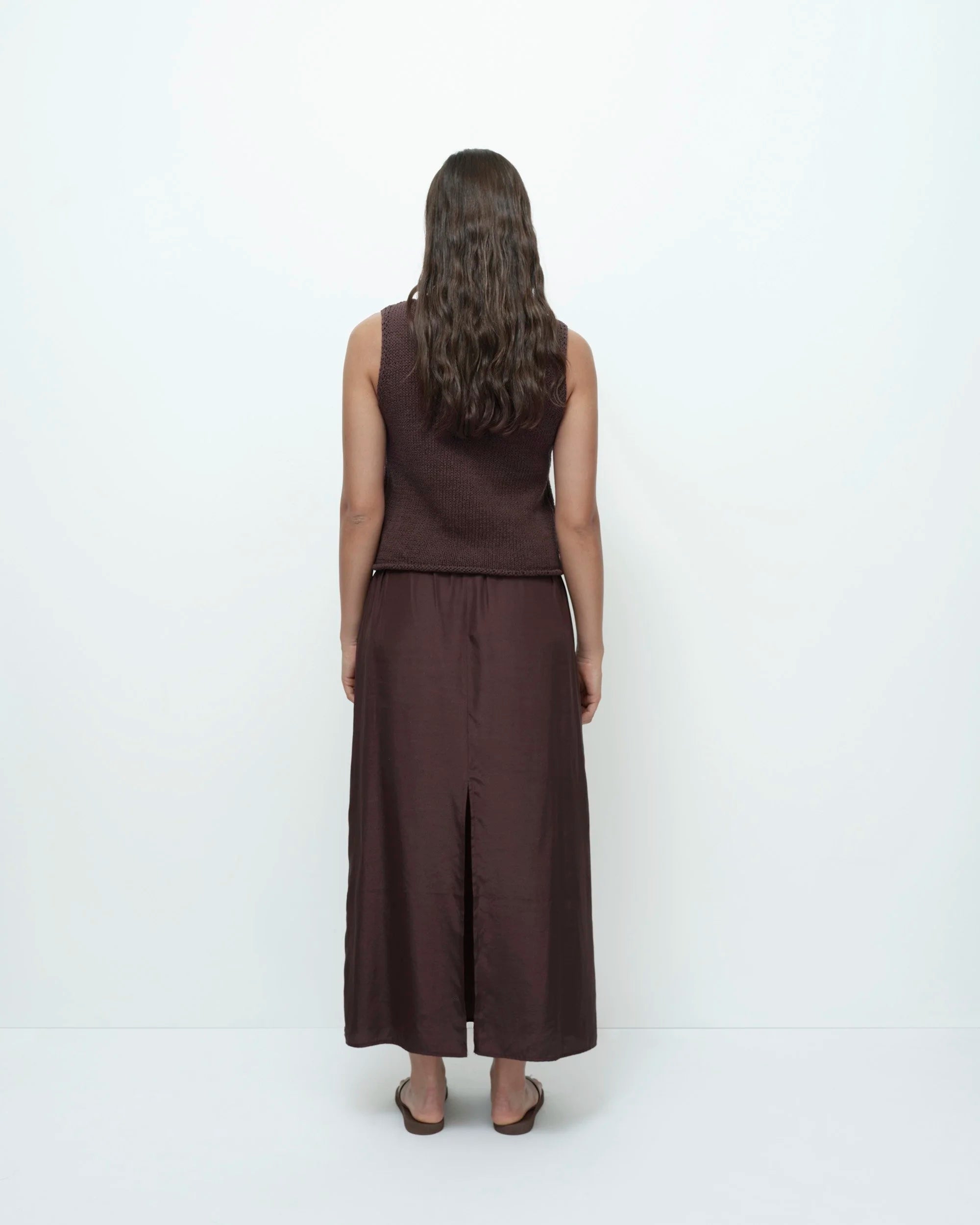 Person wearing a brown sleeveless top and wide-leg pants on a white background