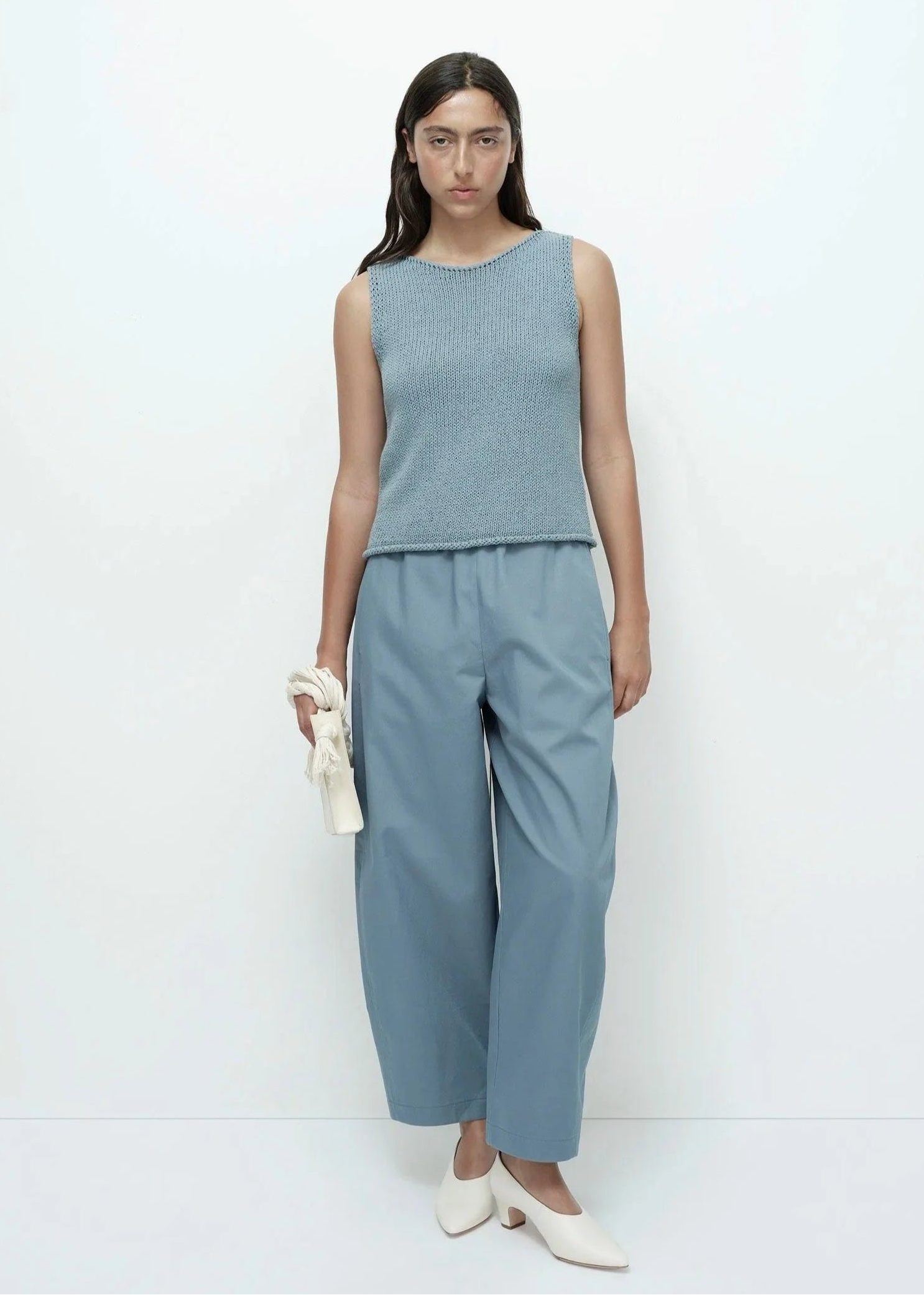 Woman wearing a sleeveless blue top and pants against a white background