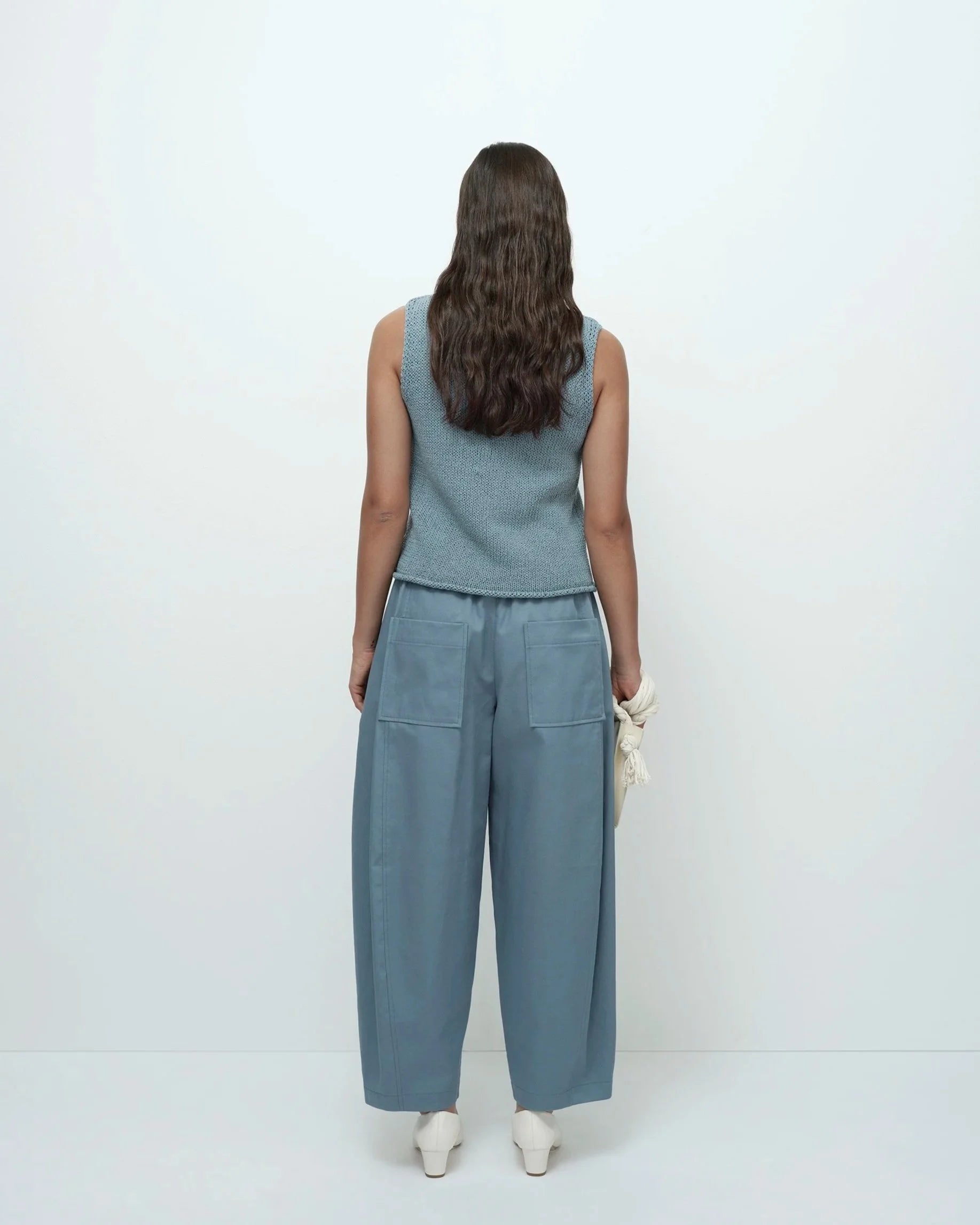 Woman wearing a blue sleeveless top and wide-leg pants on a white background