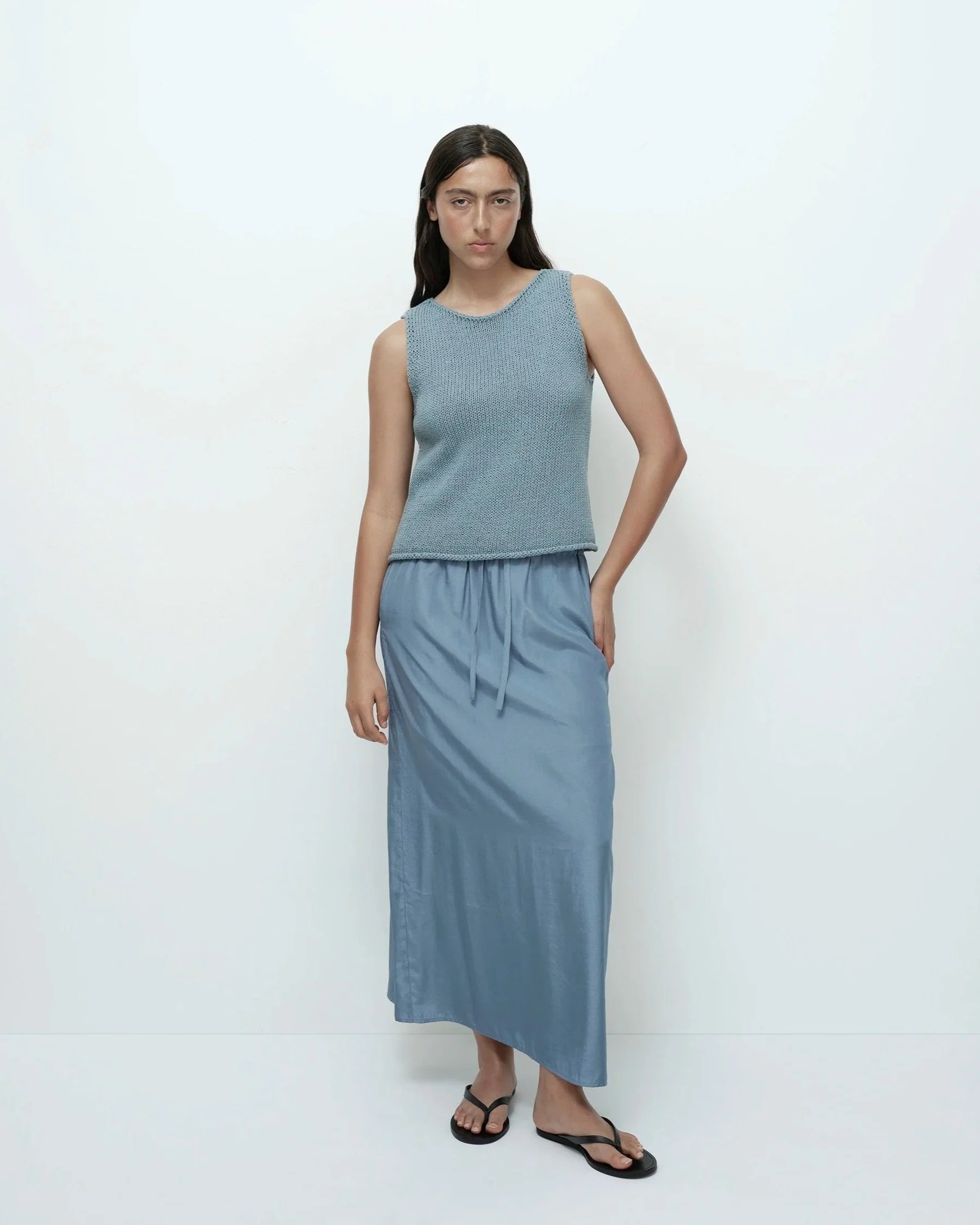 Woman wearing a light blue sleeveless top and long skirt on a white background