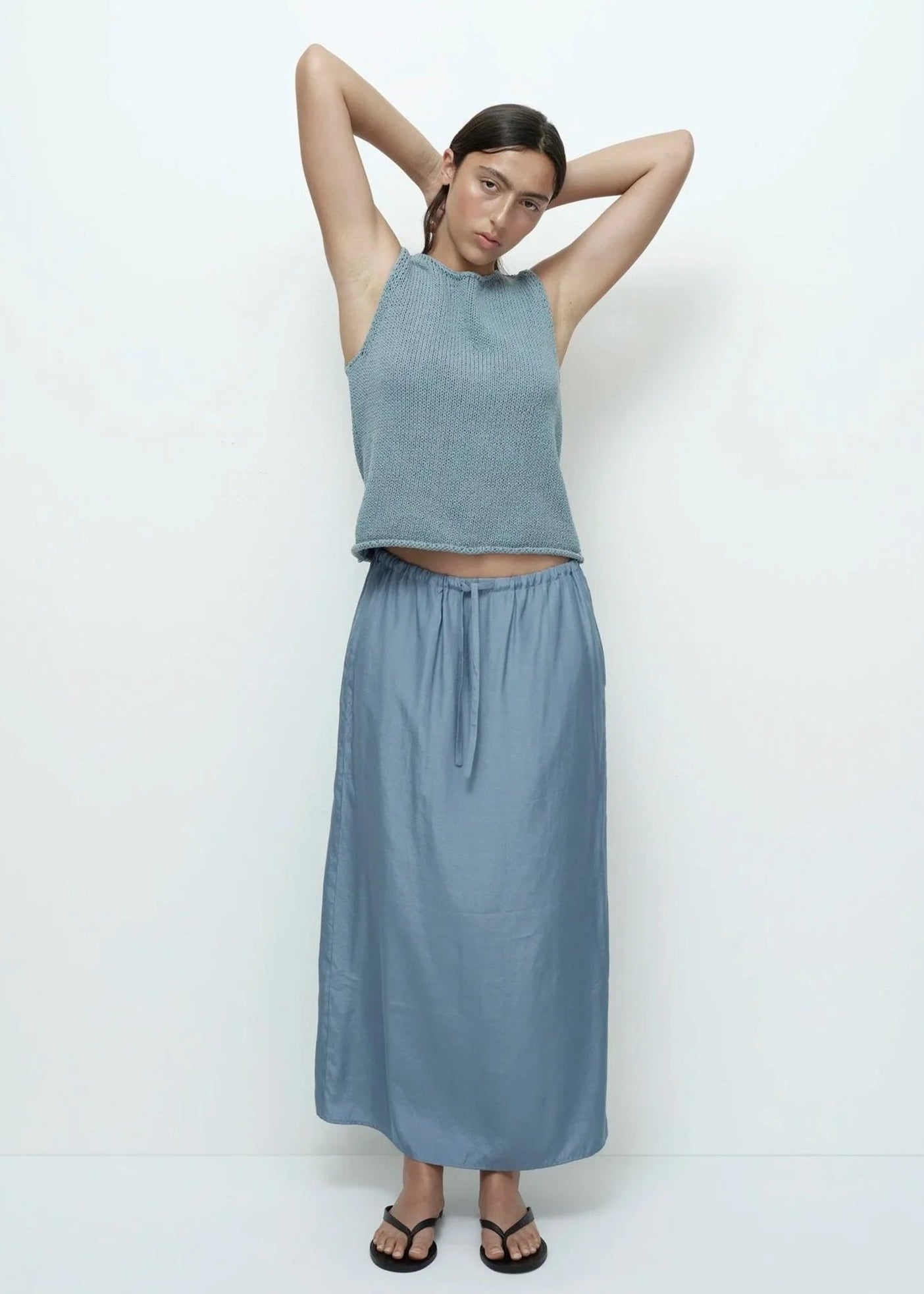 Woman wearing a light blue sleeveless top and long skirt on a white background