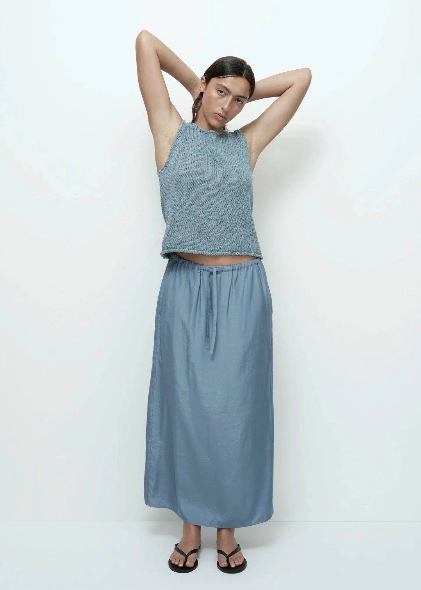 Woman wearing a blue sleeveless top and long skirt against a white background