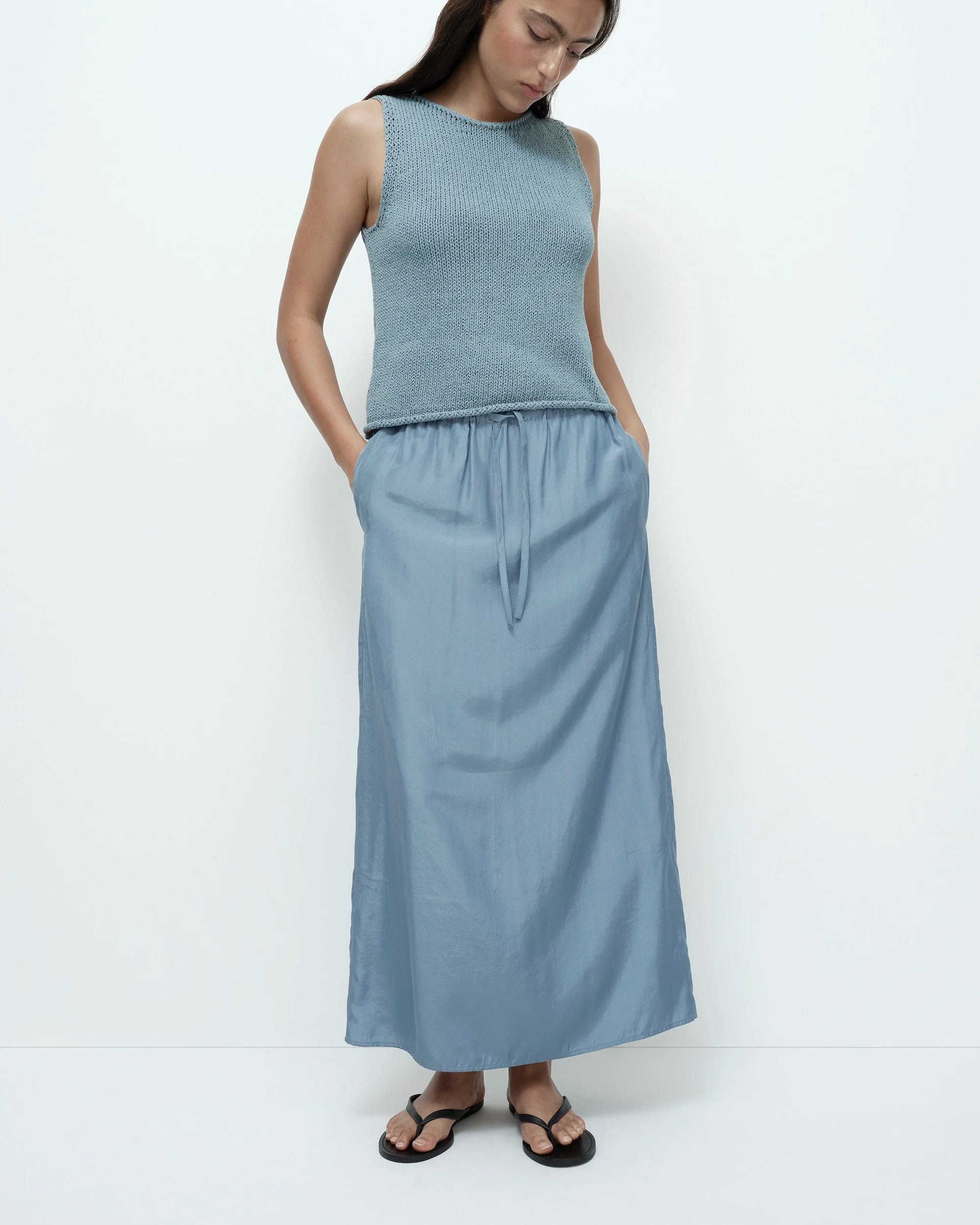 Woman wearing a light blue sleeveless top and long skirt on a white background