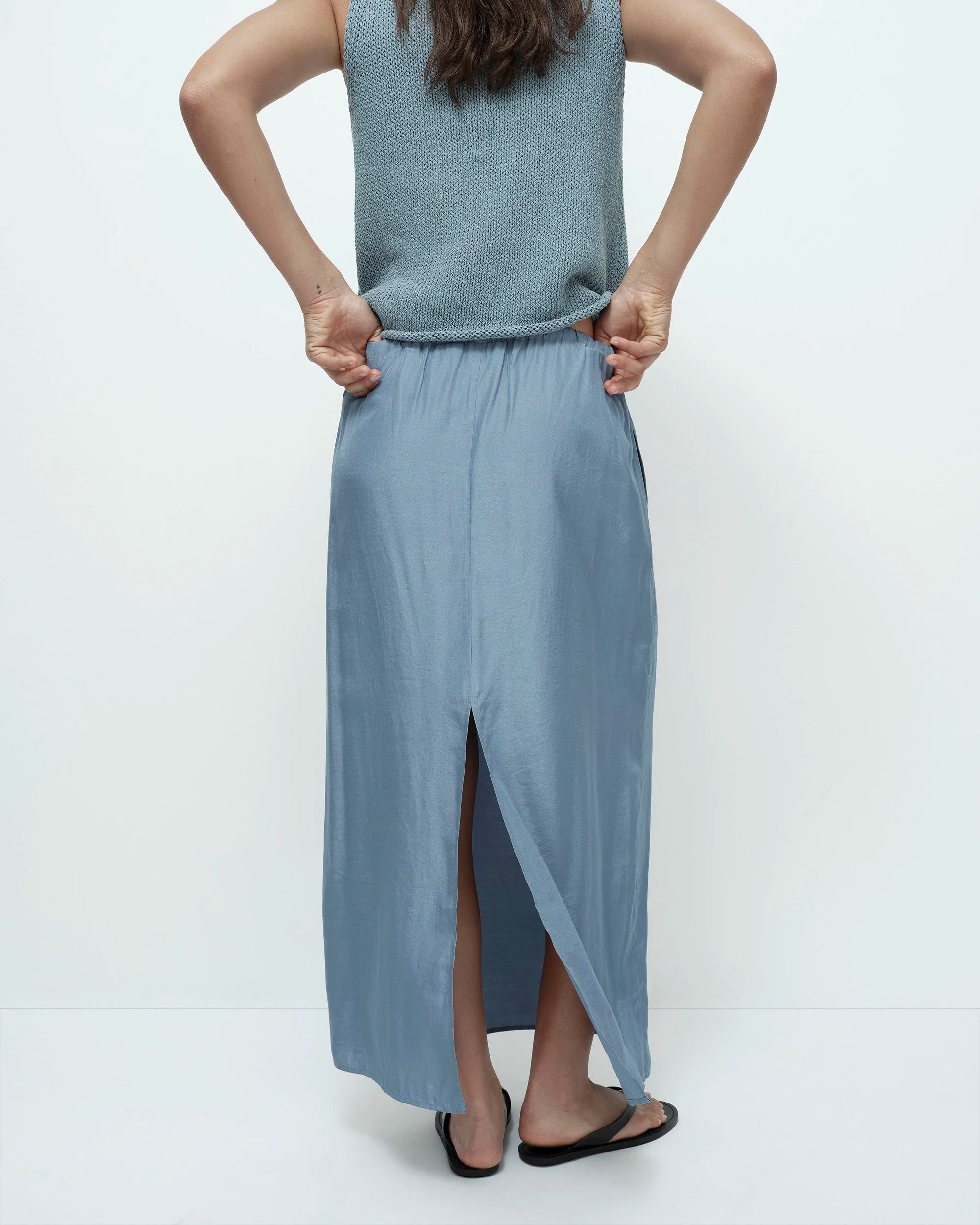 Person wearing a light blue sleeveless top and long skirt on a white background