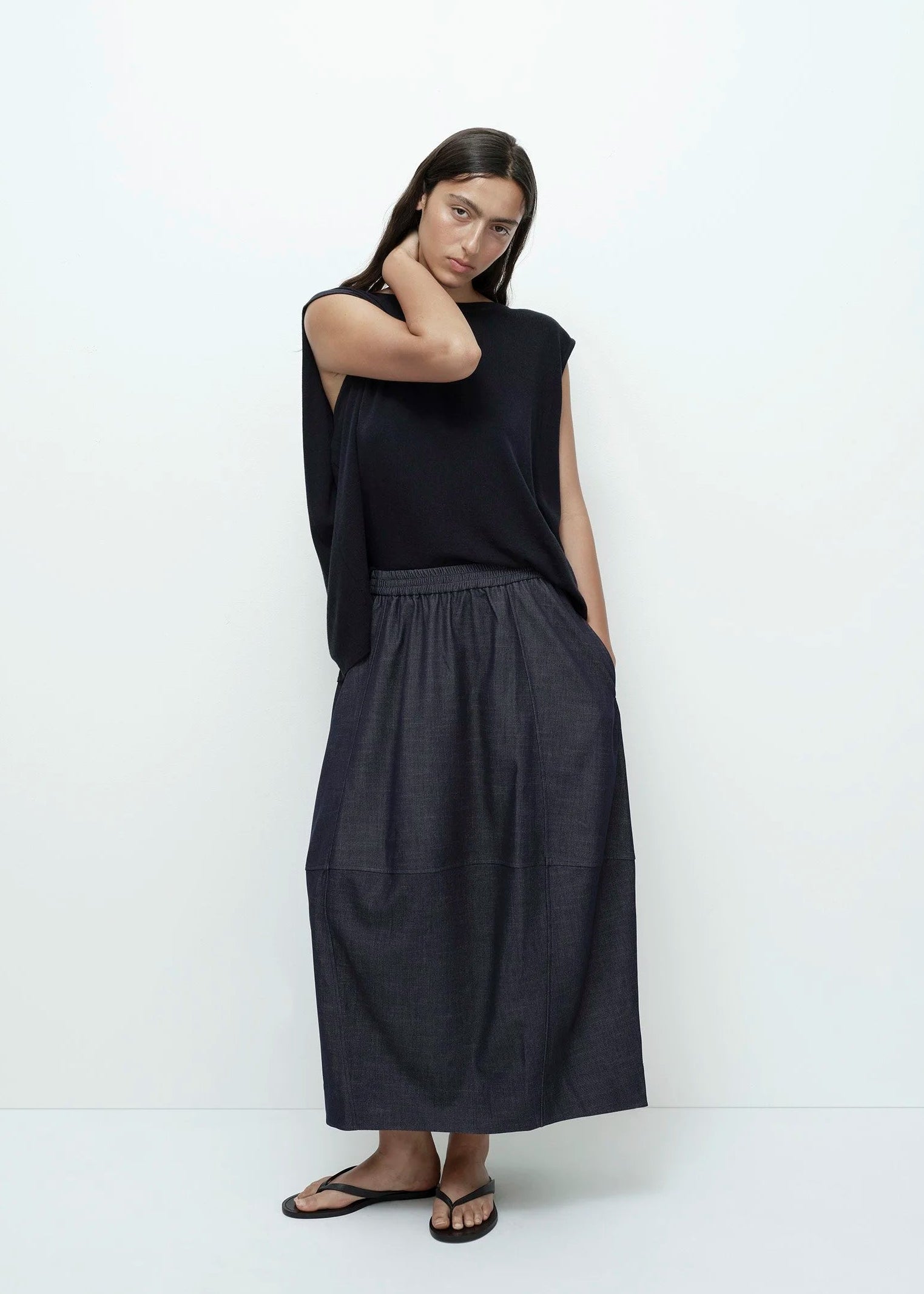 Woman wearing a black top and denim skirt with a white background