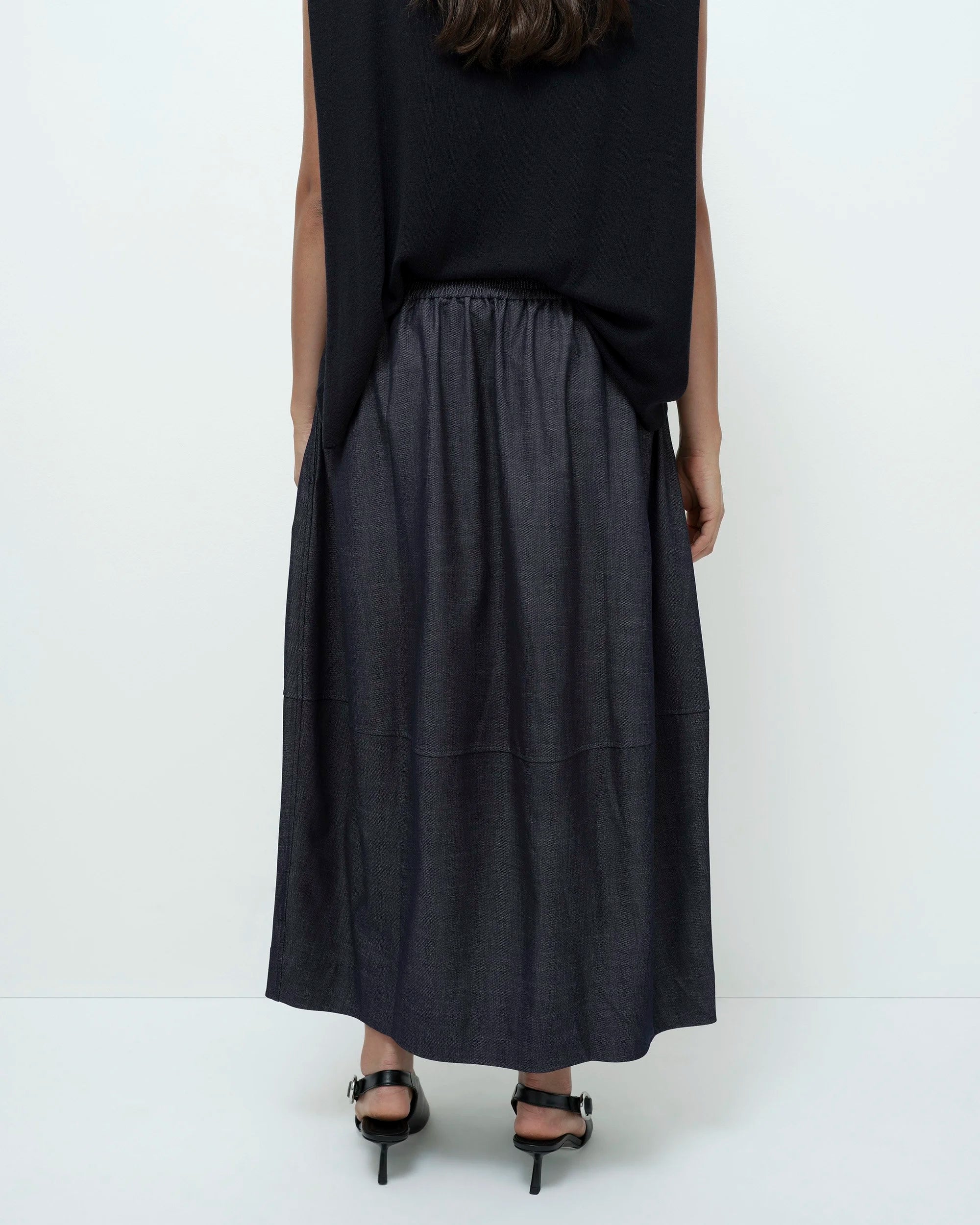 back of woman wearing a black top and denim skirt with a white background