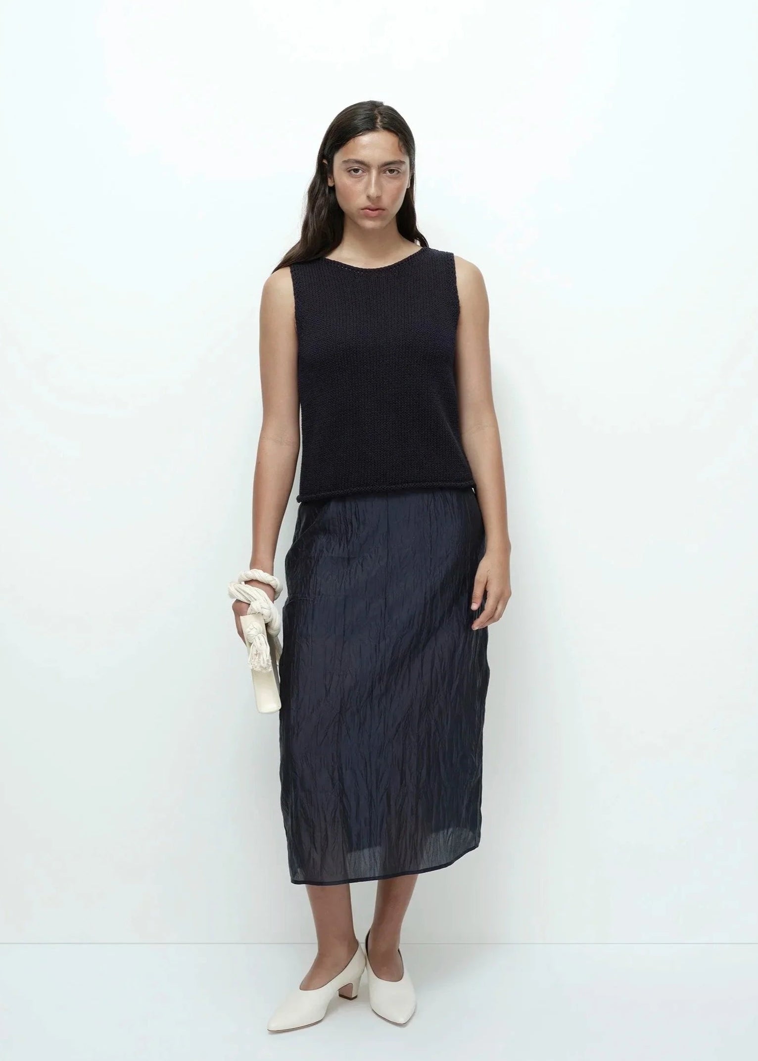 Woman wearing a black sleeveless top and dark blue skirt on a white background