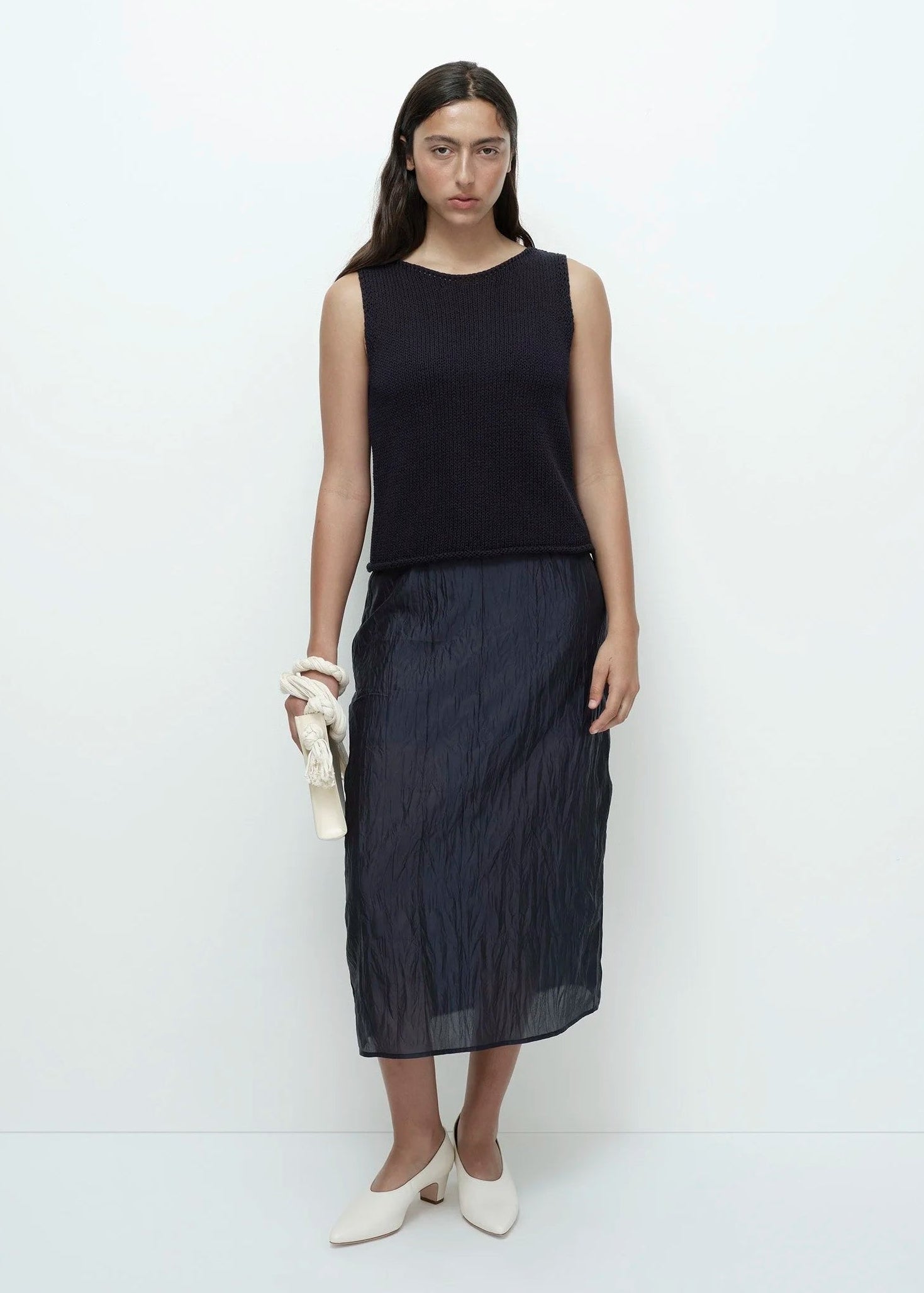 Woman wearing a navy sleeveless top and dark skirt on a white background