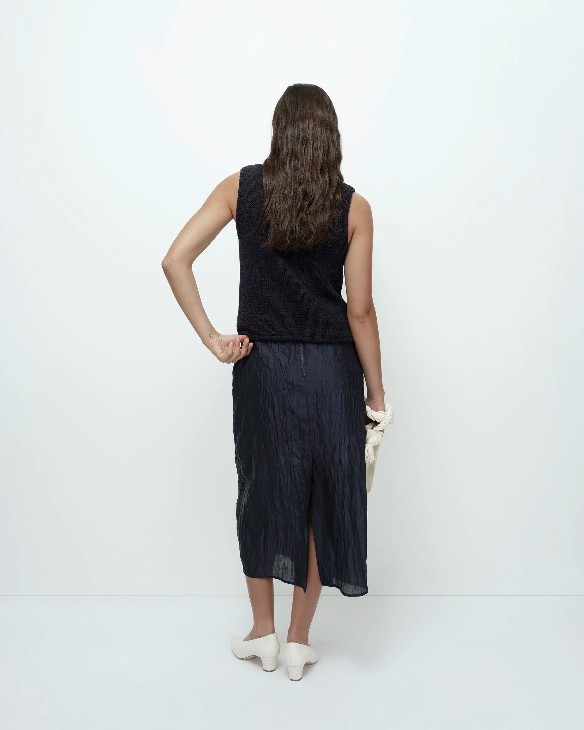 Woman wearing a navy sleeveless top and dark skirt on a white background