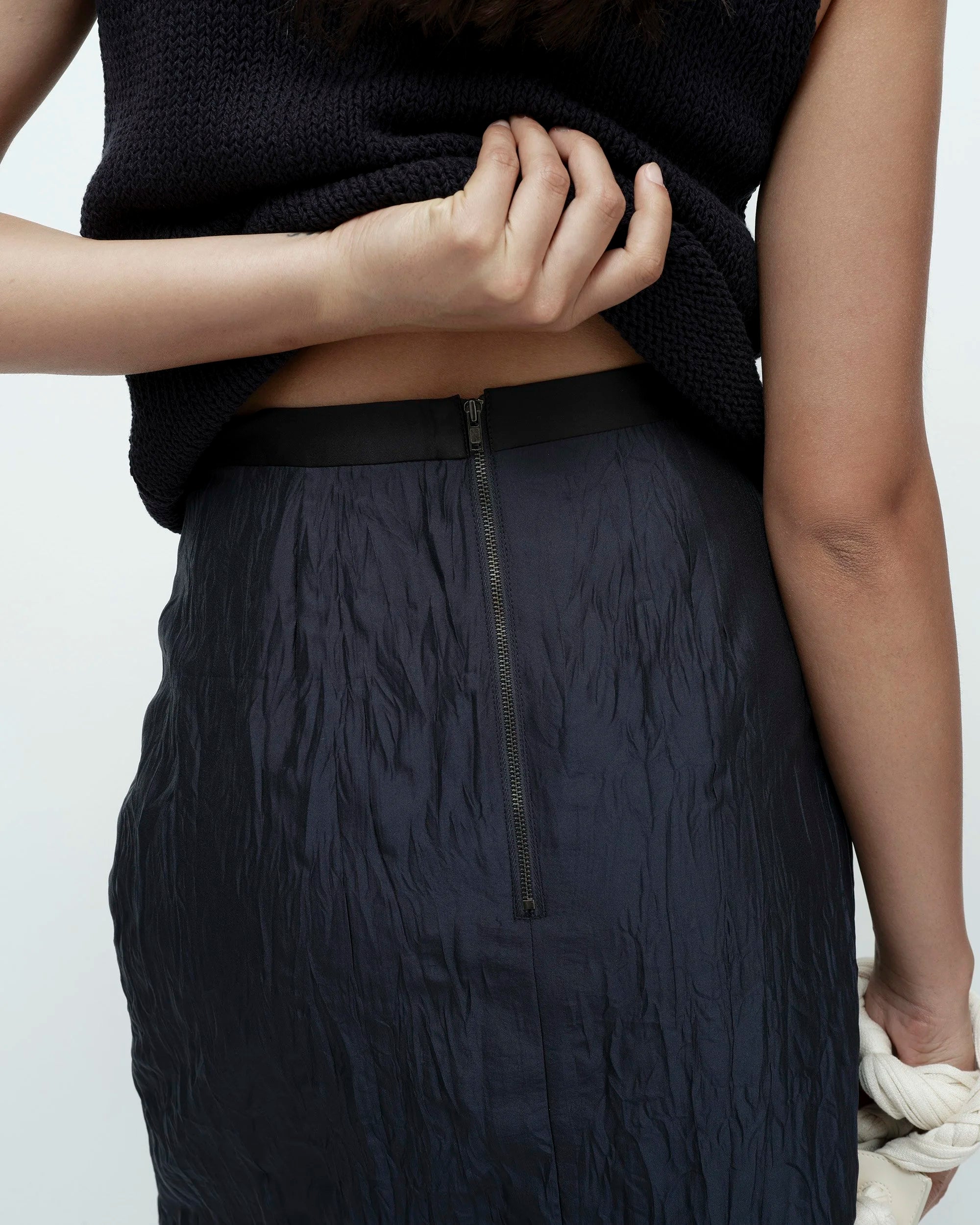 Person wearing a black textured top and navy skirt on a white background