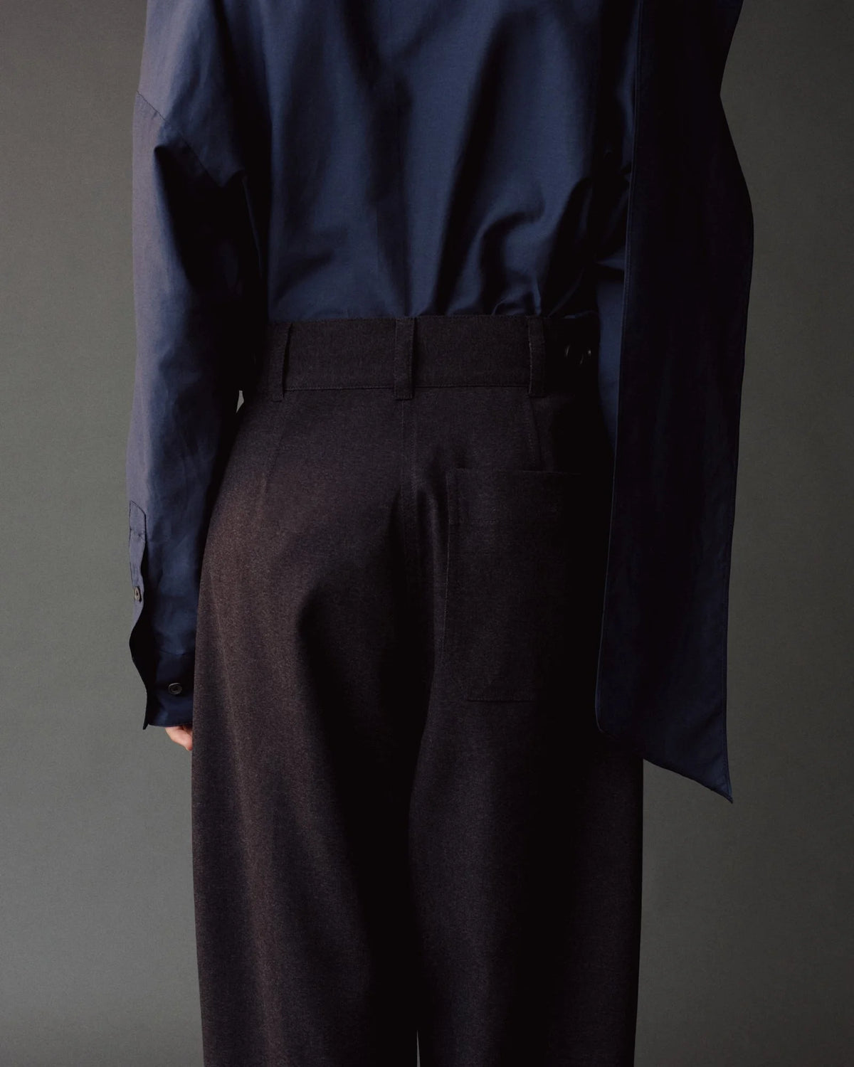 Person wearing a dark blue shirt and dark gray pants against a gray background