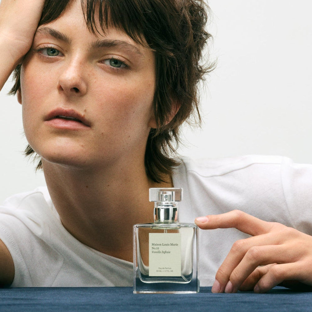 Person holding a clear perfume bottle with a silver cap on a light background