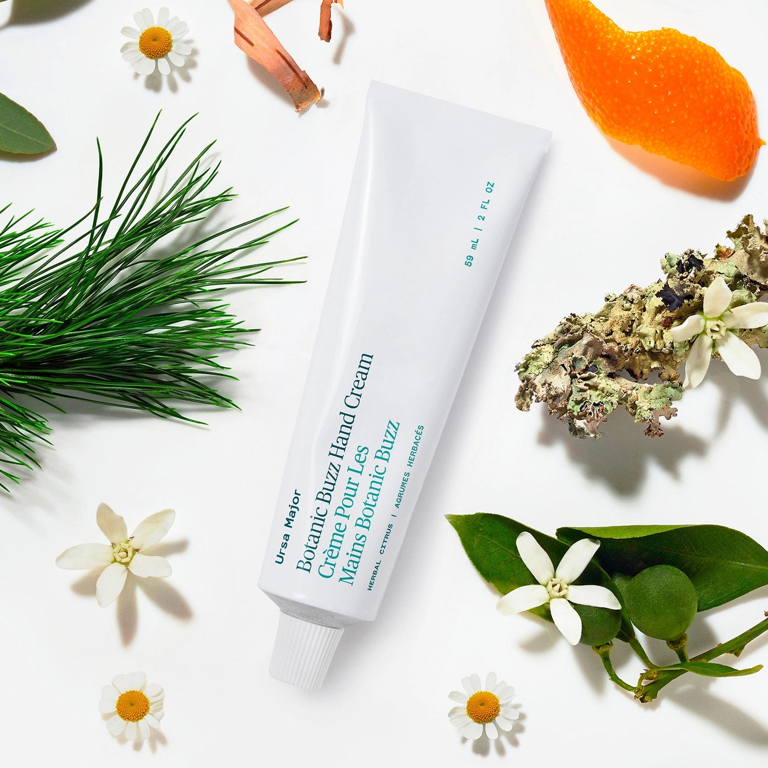 Hand cream tube labeled 'Ursa Major' surrounded by greenery and flowers on a white background