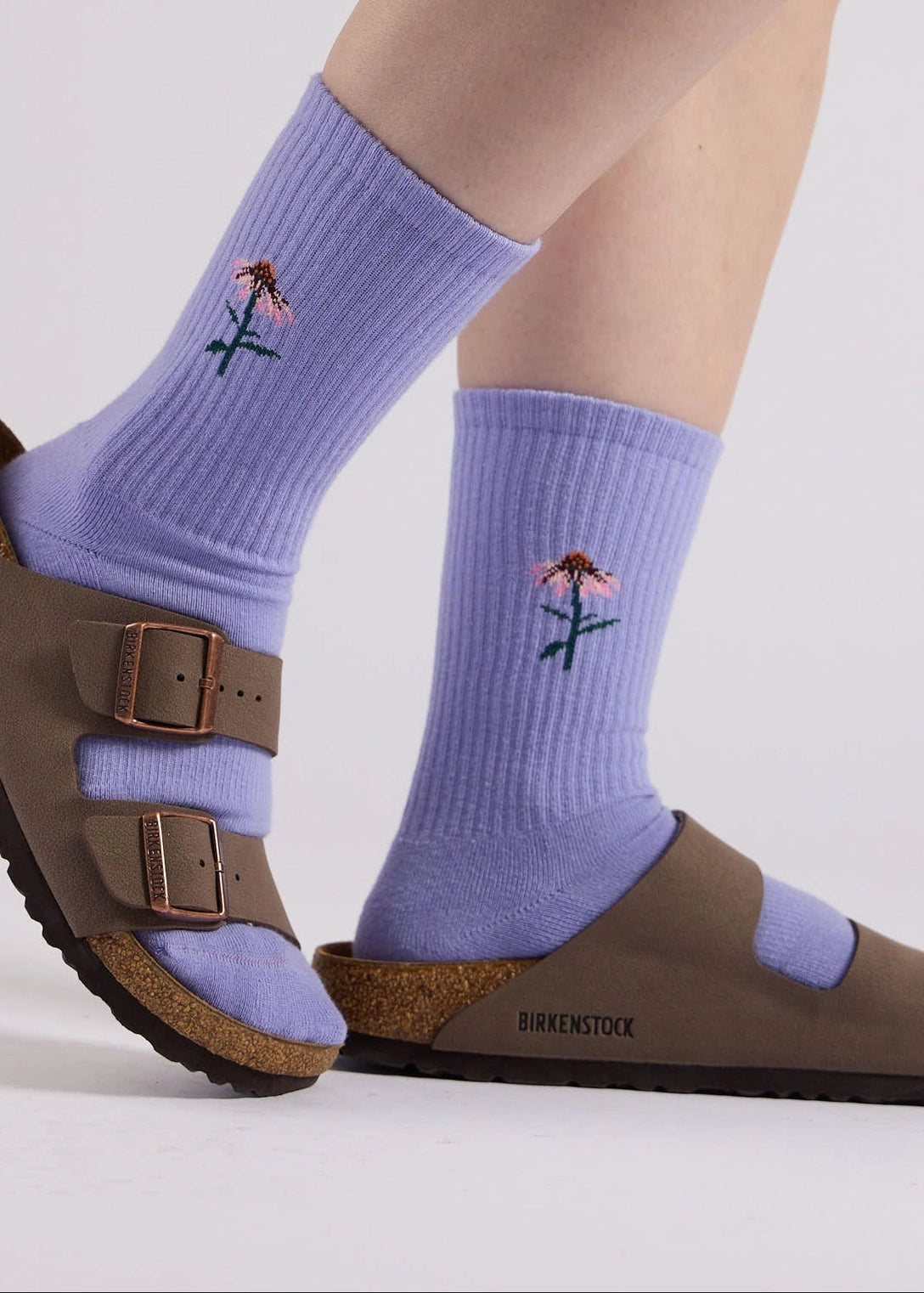 Purple socks with floral design worn with brown Birkenstock sandals on a light gray background