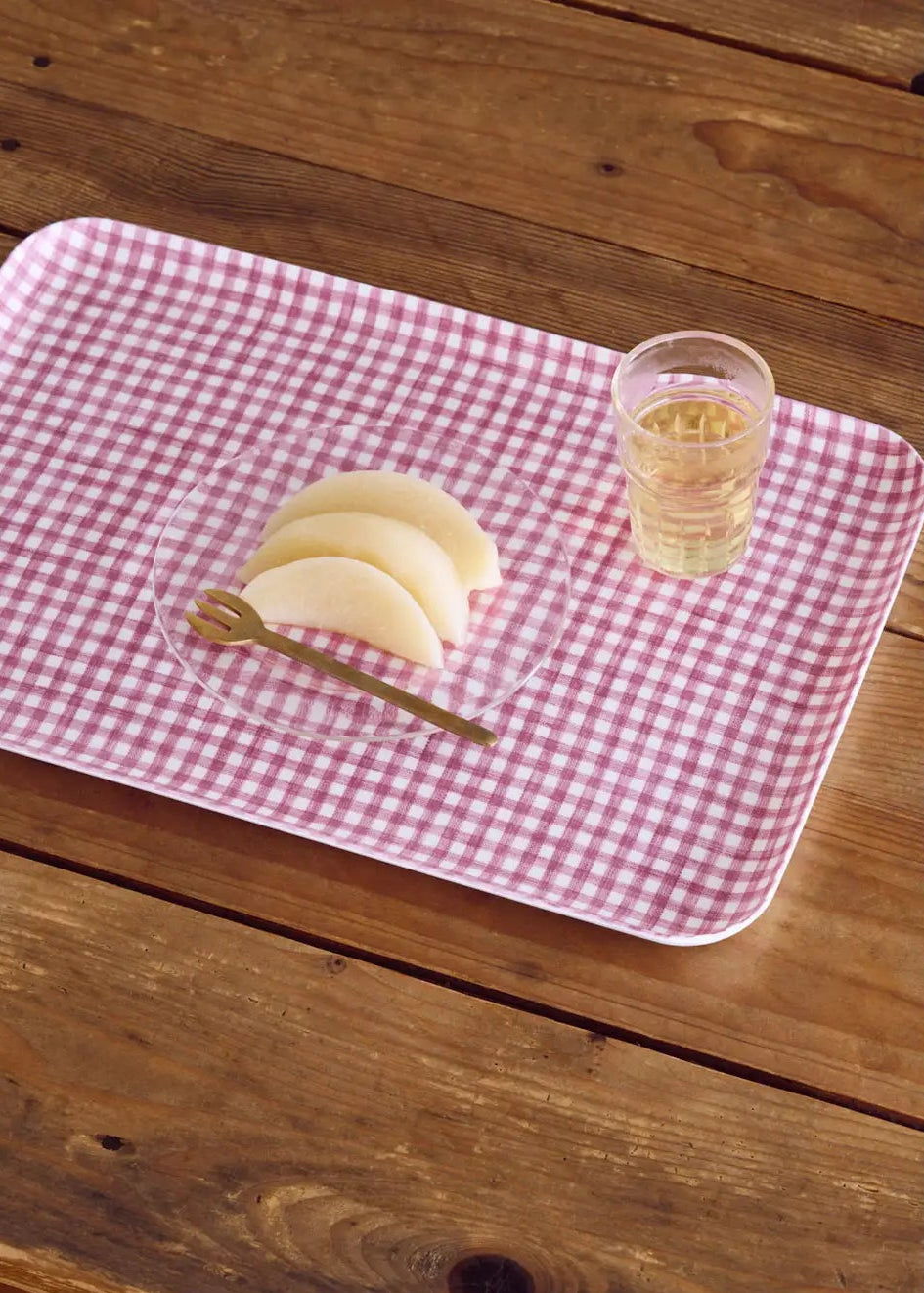Red and white checkered tray with a glass of juice and a plate of food on a wooden surface