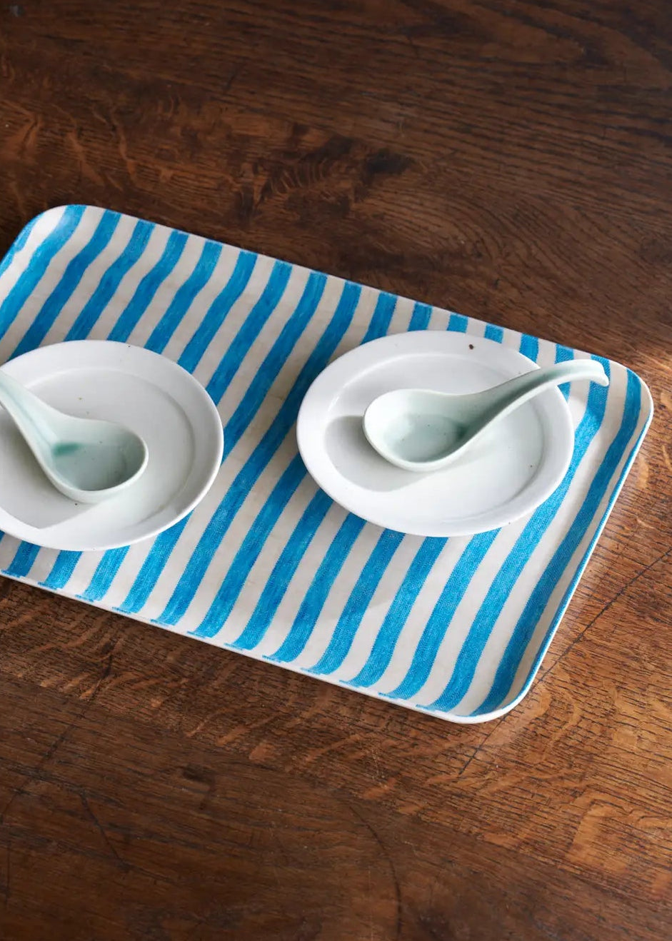 Two white bowls with spoons on a blue and white striped tray on a wooden surface