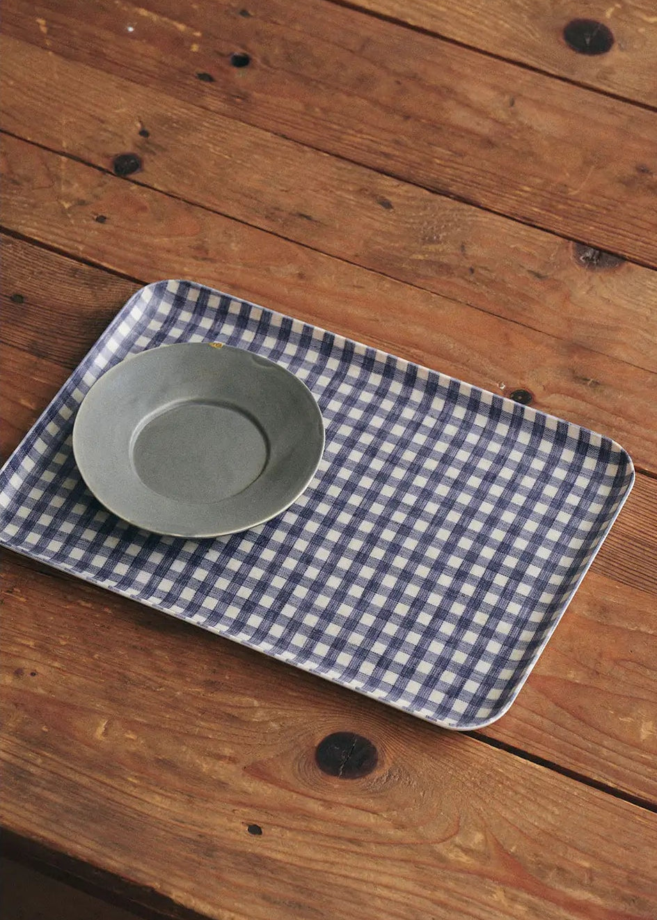 checkered tray with gray saucer on top on a wooden table