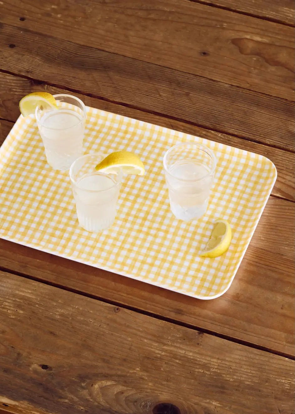 Three margaritas with lemon wedges on a yellow checkered tray on a wooden surface