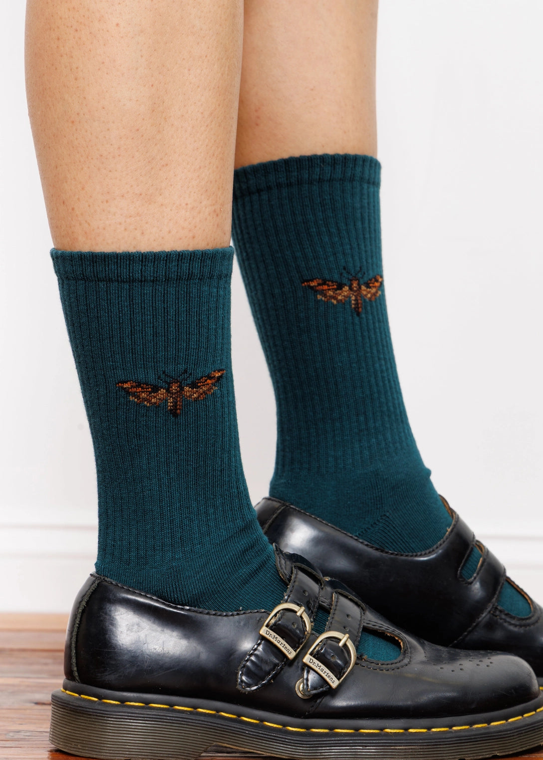 Teal socks with butterfly design worn with black shoes on a light background