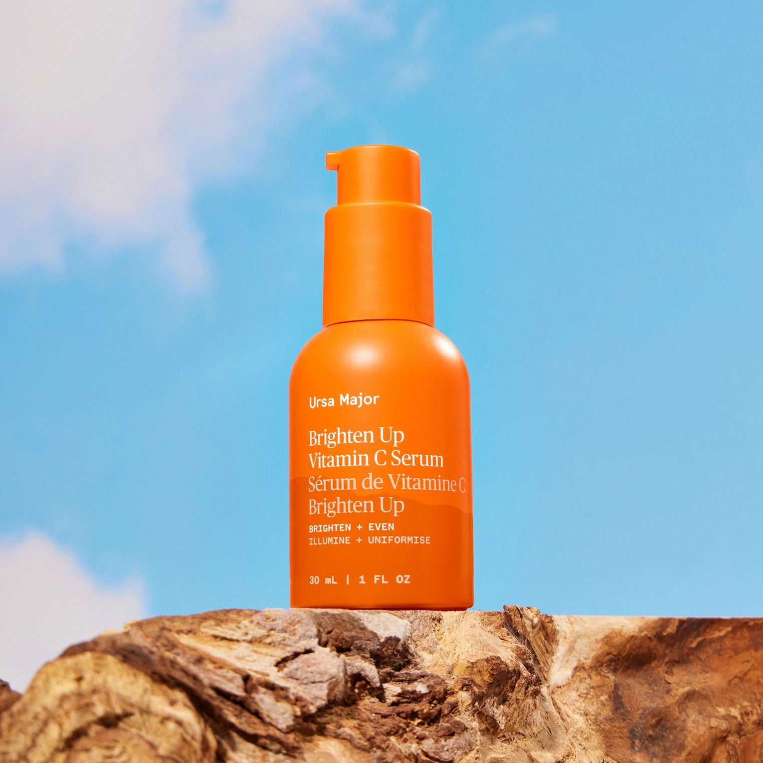 Orange bottle of Ursaa Major Vitamin C Serum on a wooden surface with a blue sky background