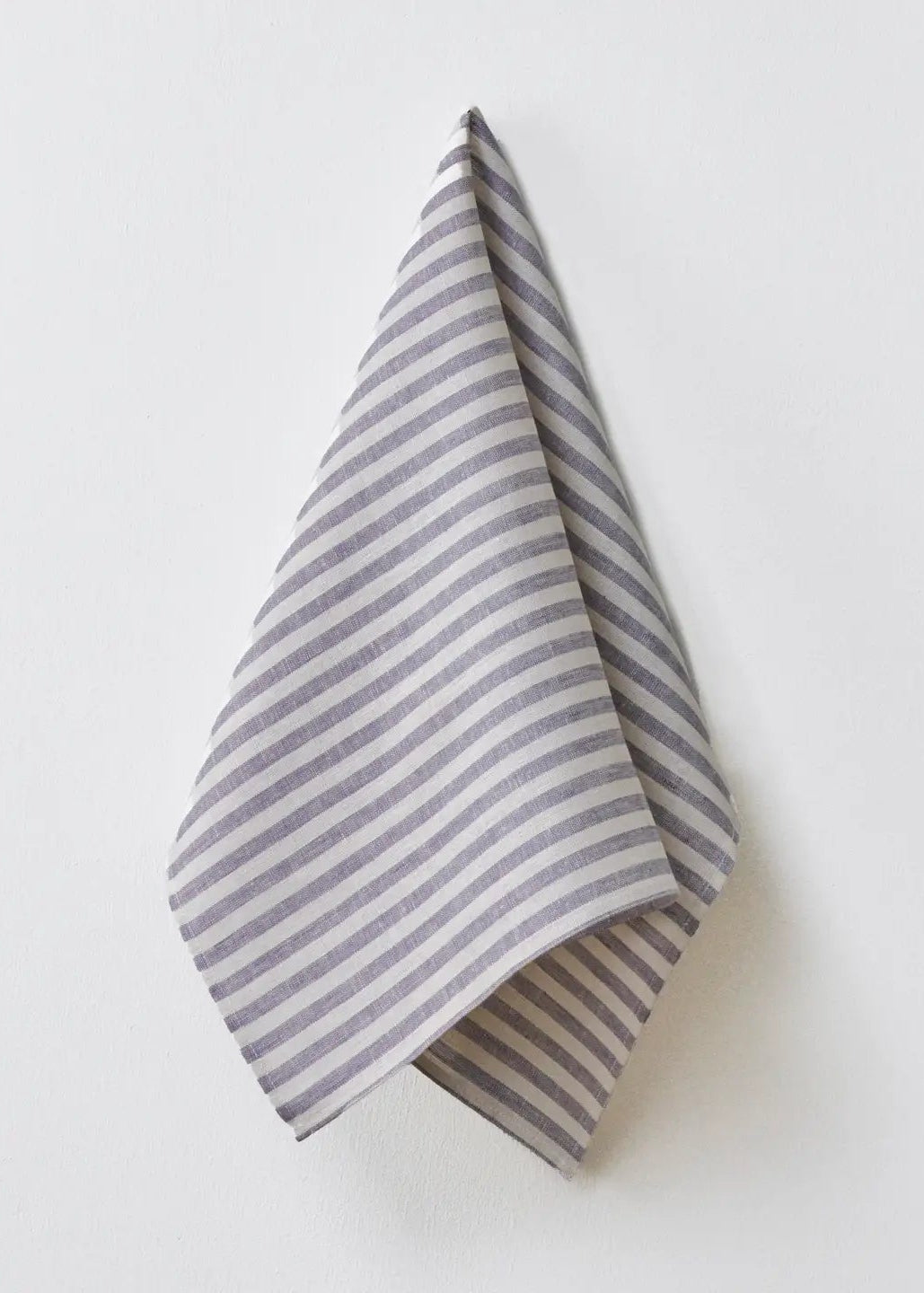 A folded striped cloth napkin or tea towel with thin gray and white horizontal stripes, hanging against a plain off-white wall.