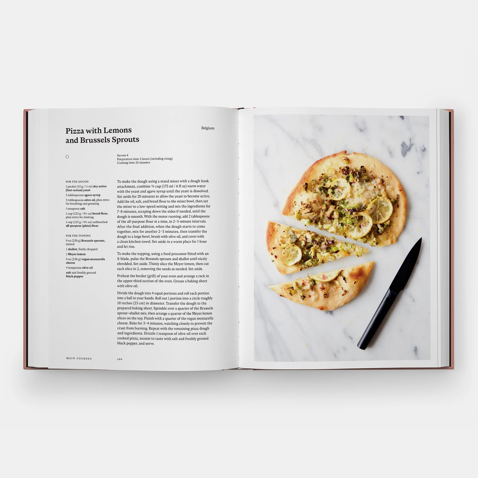 Open cookbook showing a pizza recipe with a sliced pizza on a marble surface.