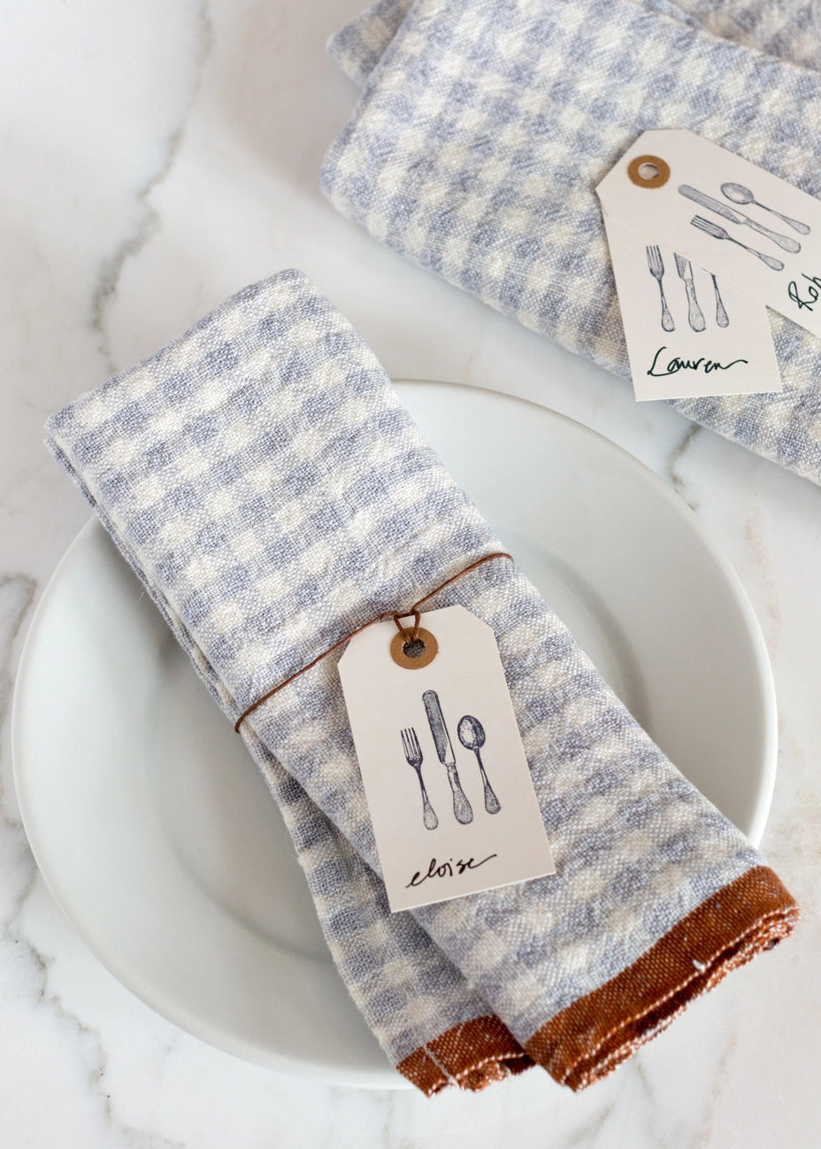 Blue and white checkered napkins with brown trim on a white plate, accompanied by tags.