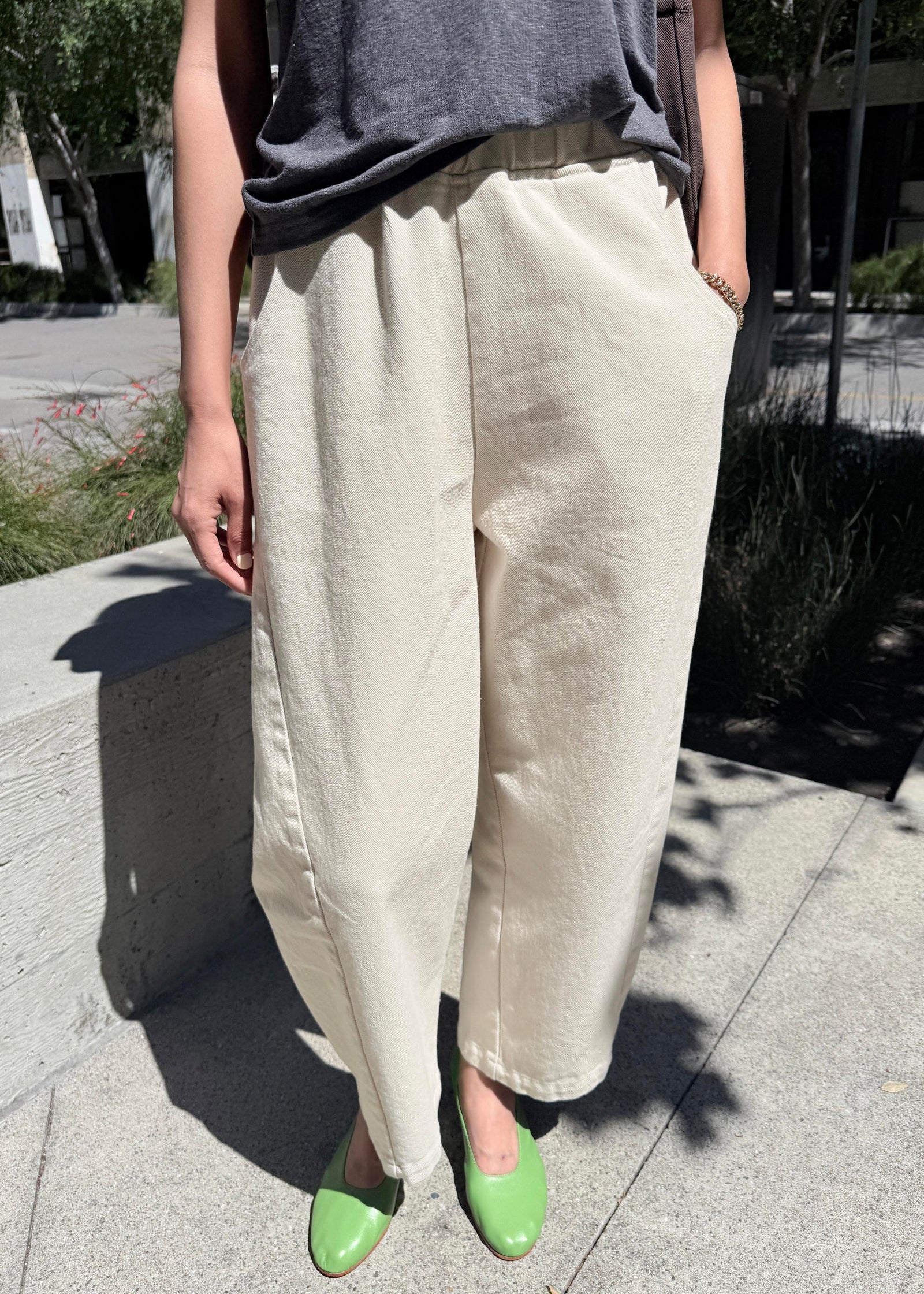 Person wearing beige wide-leg pants and green shoes on a sidewalk.
