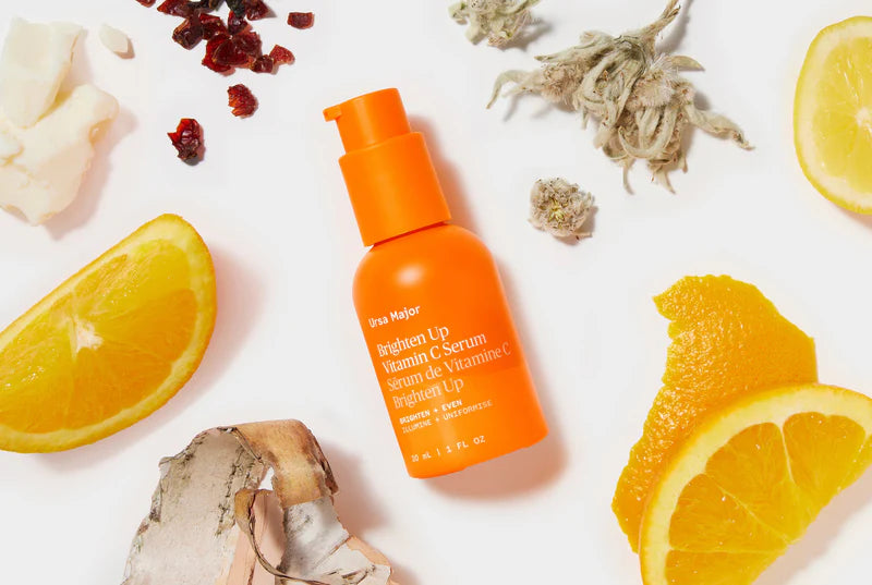 Orange serum bottle on a white background with orange slices and dried herbs
