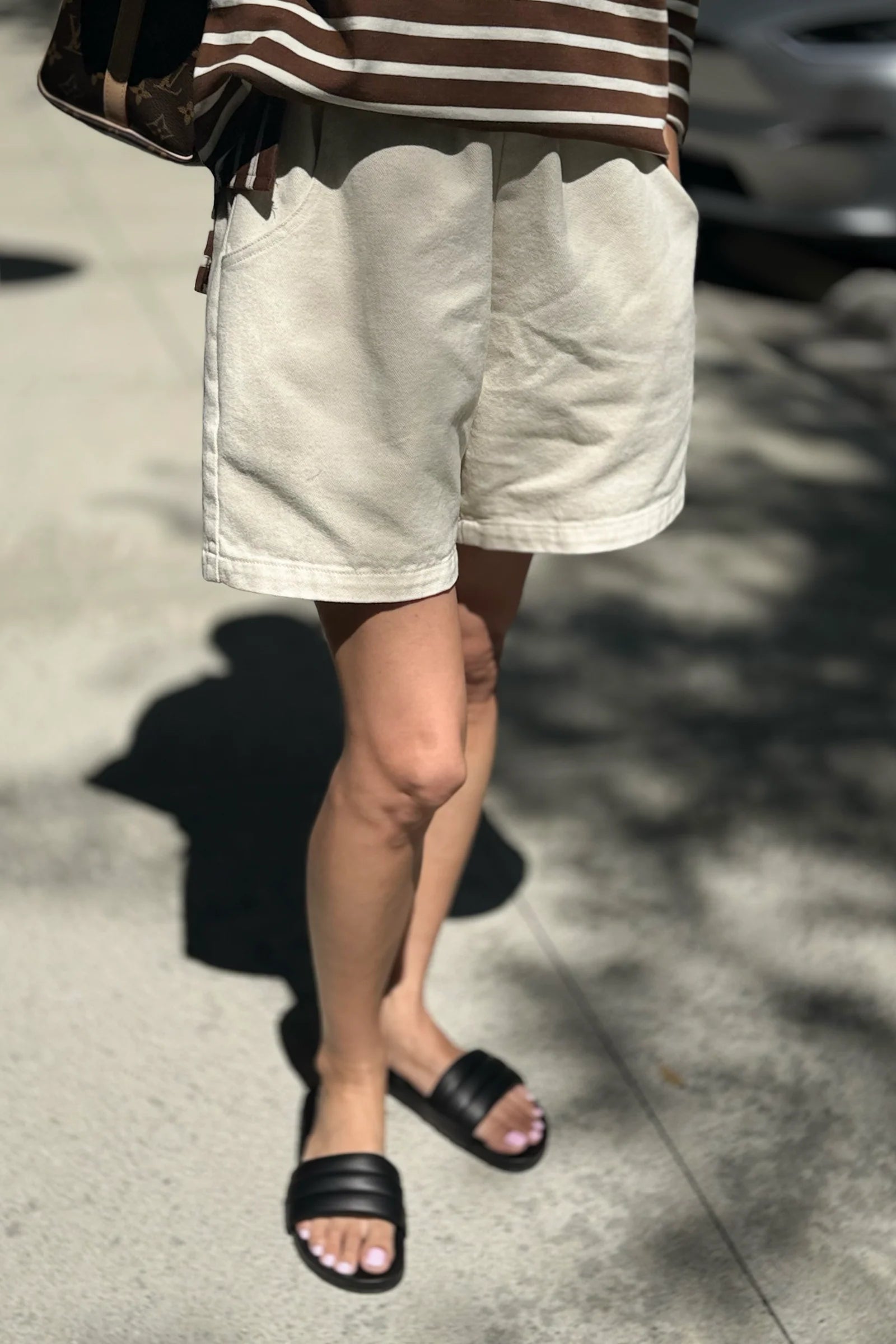 Person wearing white shorts and black sandals on a street.