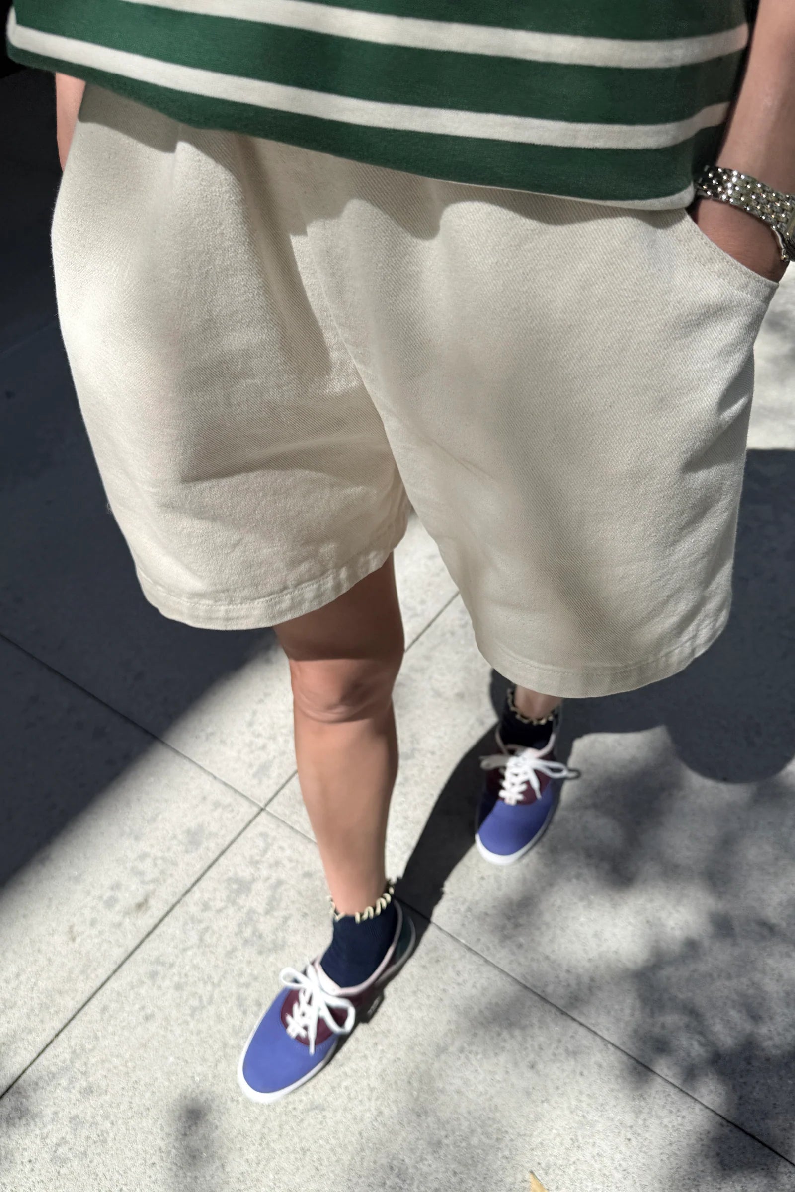 Person wearing a green and white striped shirt, beige shorts, and blue sneakers on a concrete surface.