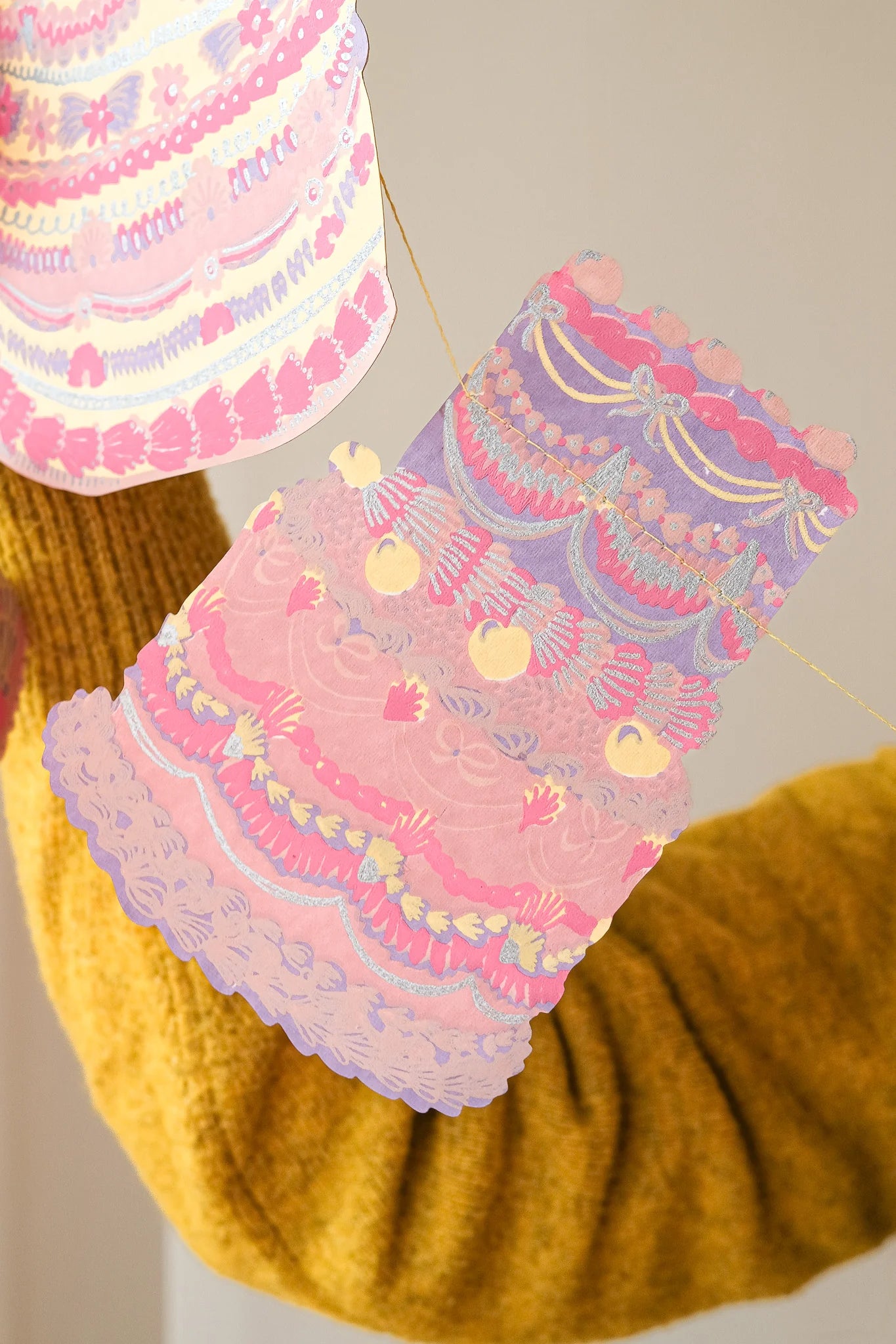 Decorative paper cake with pink and purple layers on a yellow knitted surface