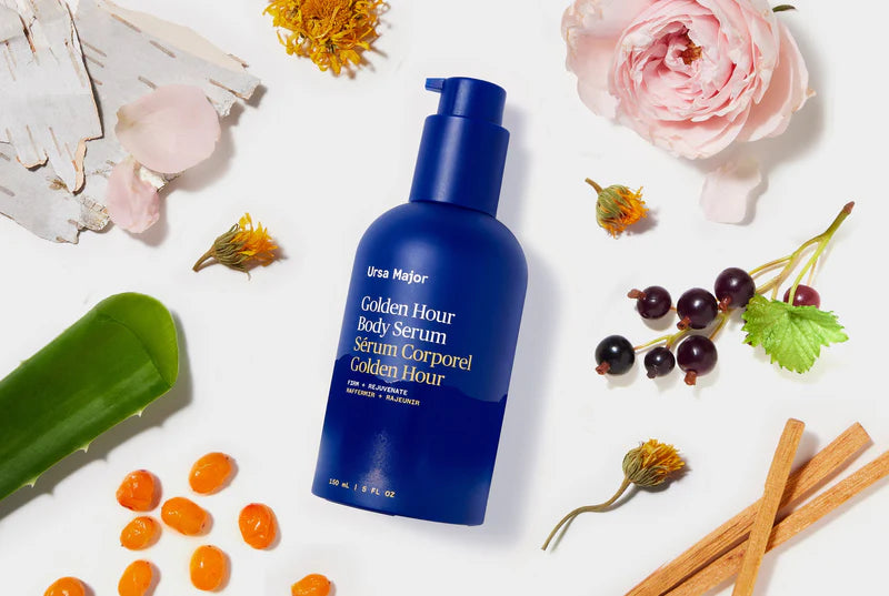 Blue bottle of Golden Hour Body Serum surrounded by flowers and herbs on a white background