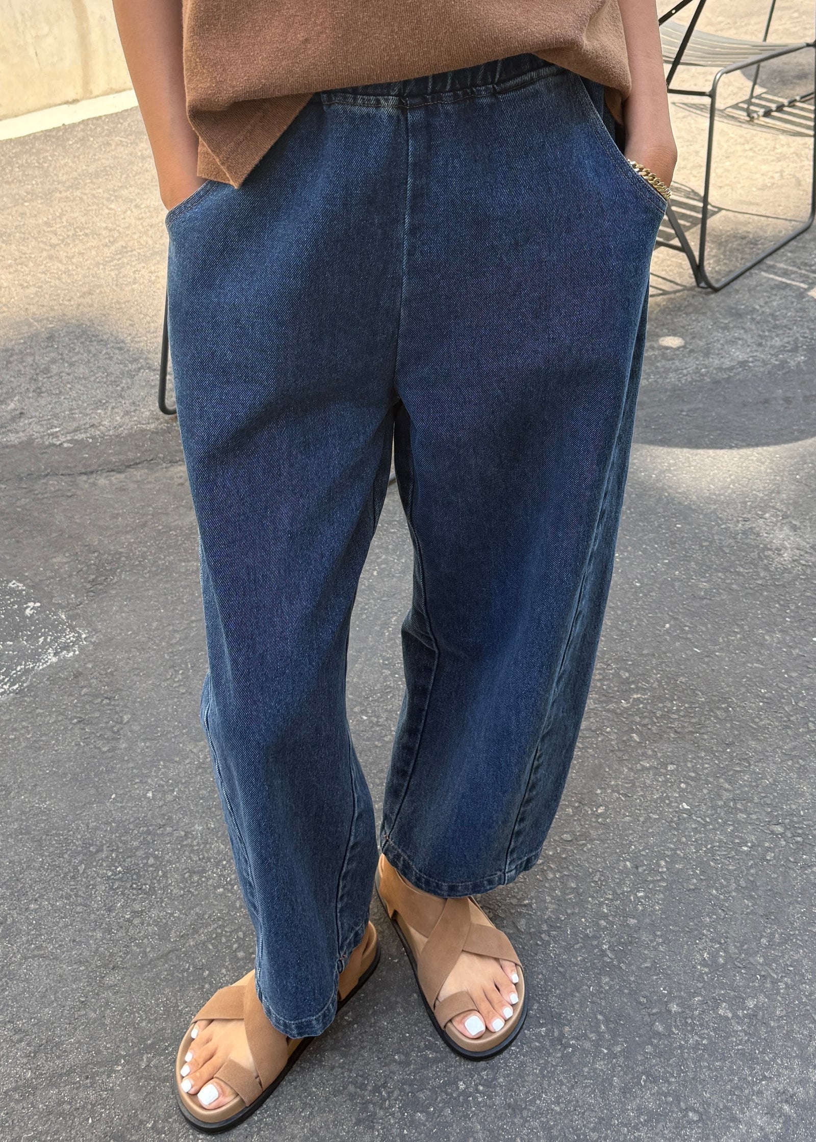 Person wearing blue jeans and a brown top on a street.