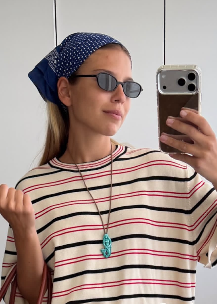 Woman taking a selfie wearing a striped shirt and sunglasses, holding a woven bag.