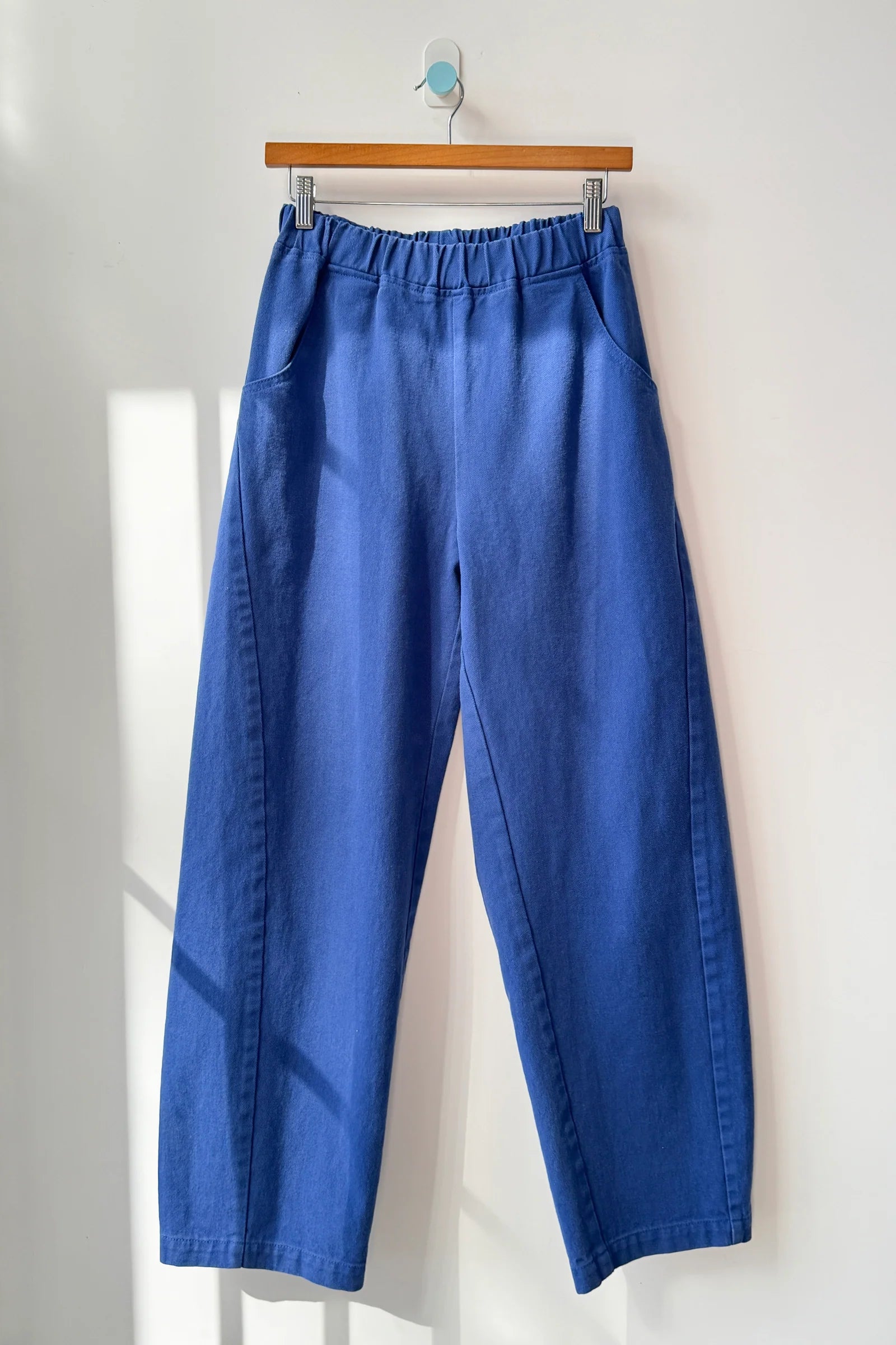 Blue pants hanging on a wooden hanger against a white wall.