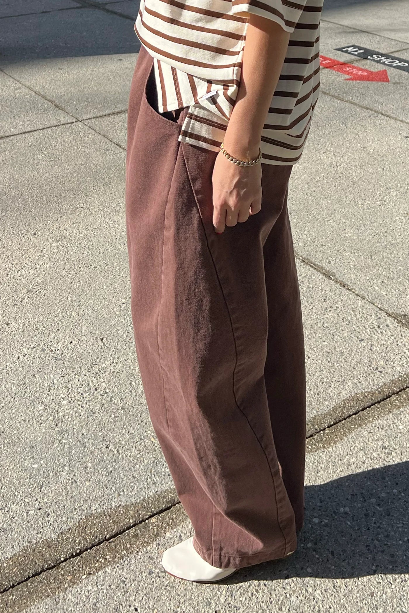Person wearing brown wide-leg pants and a striped shirt on a pavement.