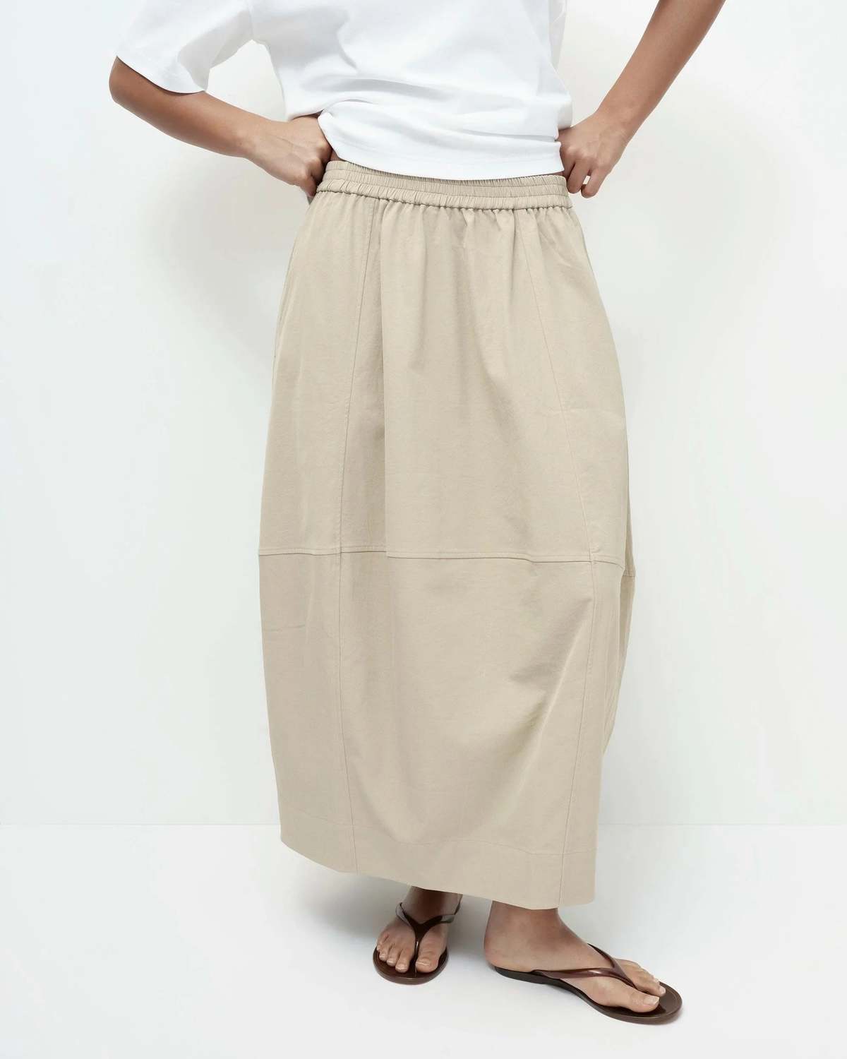 Person wearing a beige skirt and white top on a white background