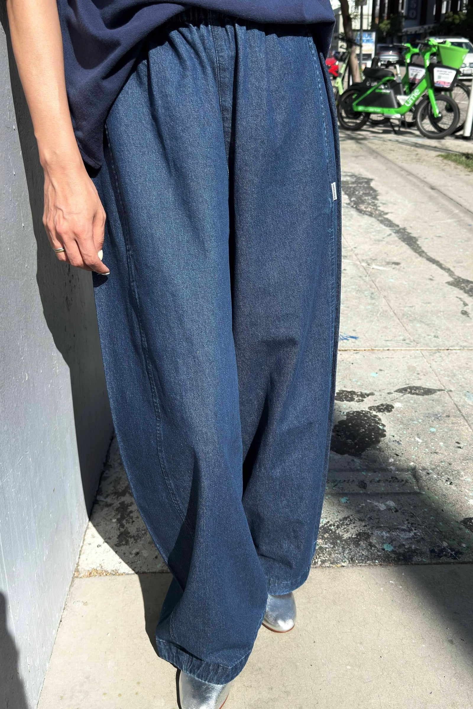 Person wearing blue wide-leg jeans on a sidewalk.