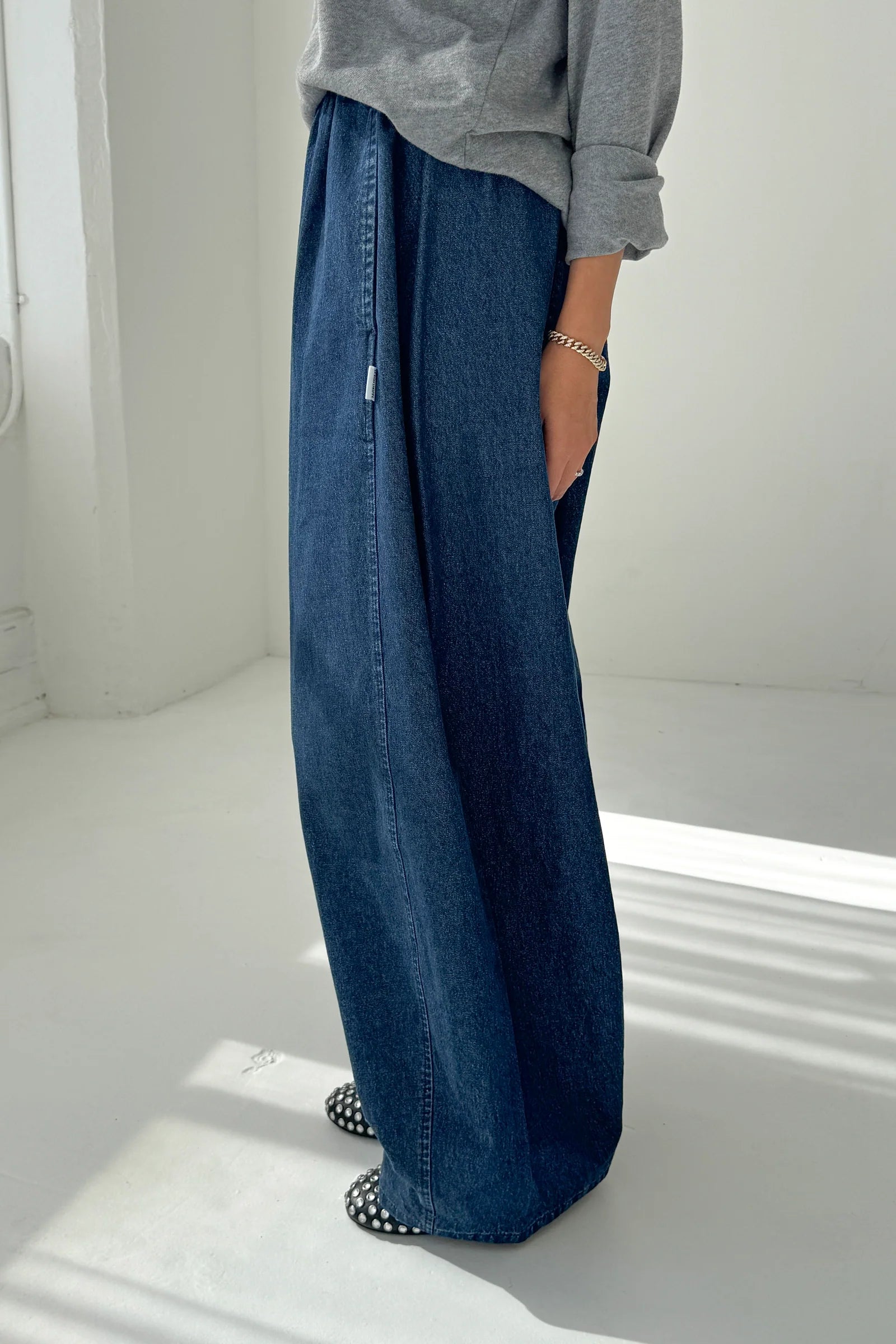 Person wearing blue wide-leg jeans and a gray top on a white background