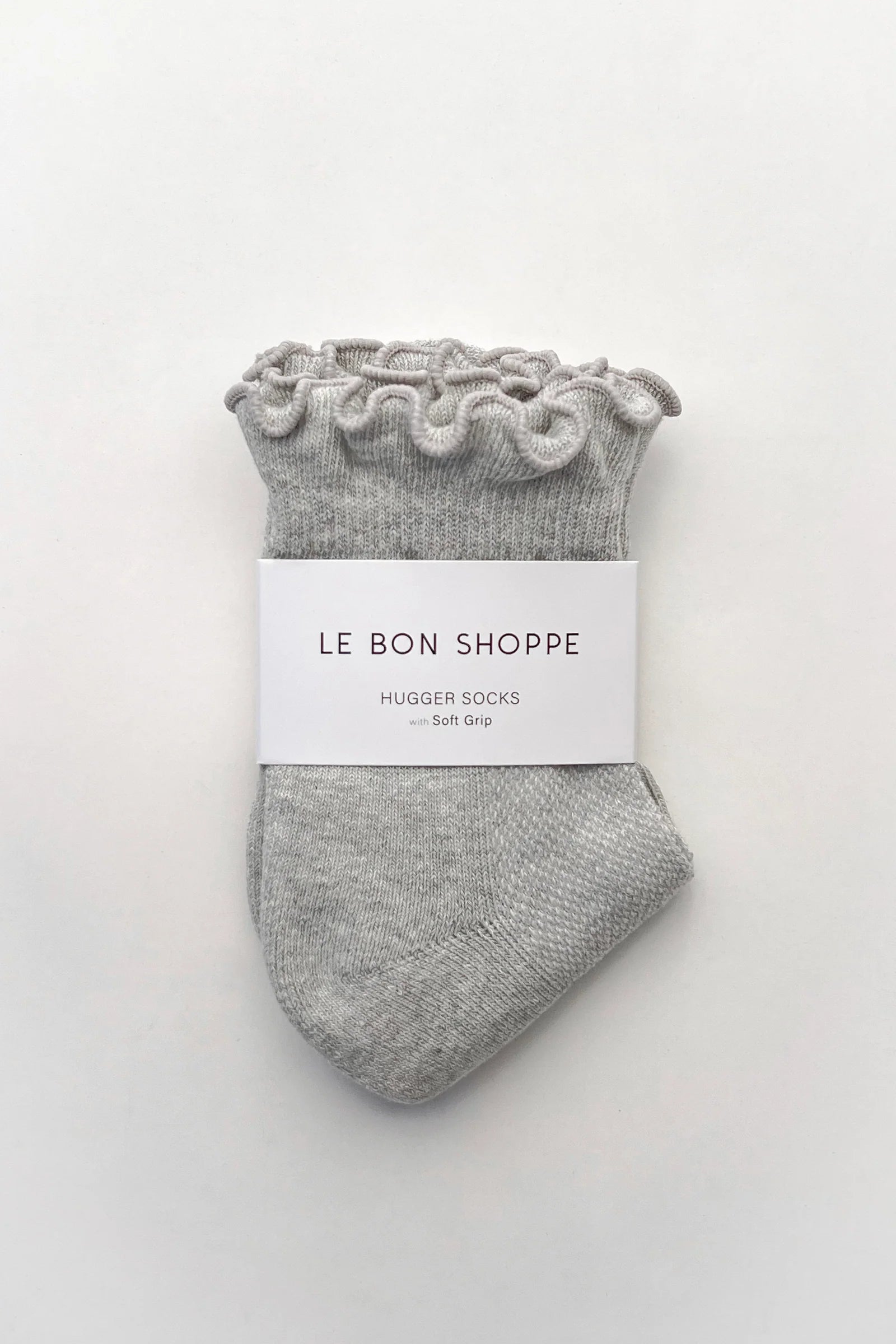 A pair of light gray knit huggie socks with ruffled cuffs, wrapped in a white paper band labeled 'LE BON SHOPPE HUGGER SOCKS - Soft gray'.